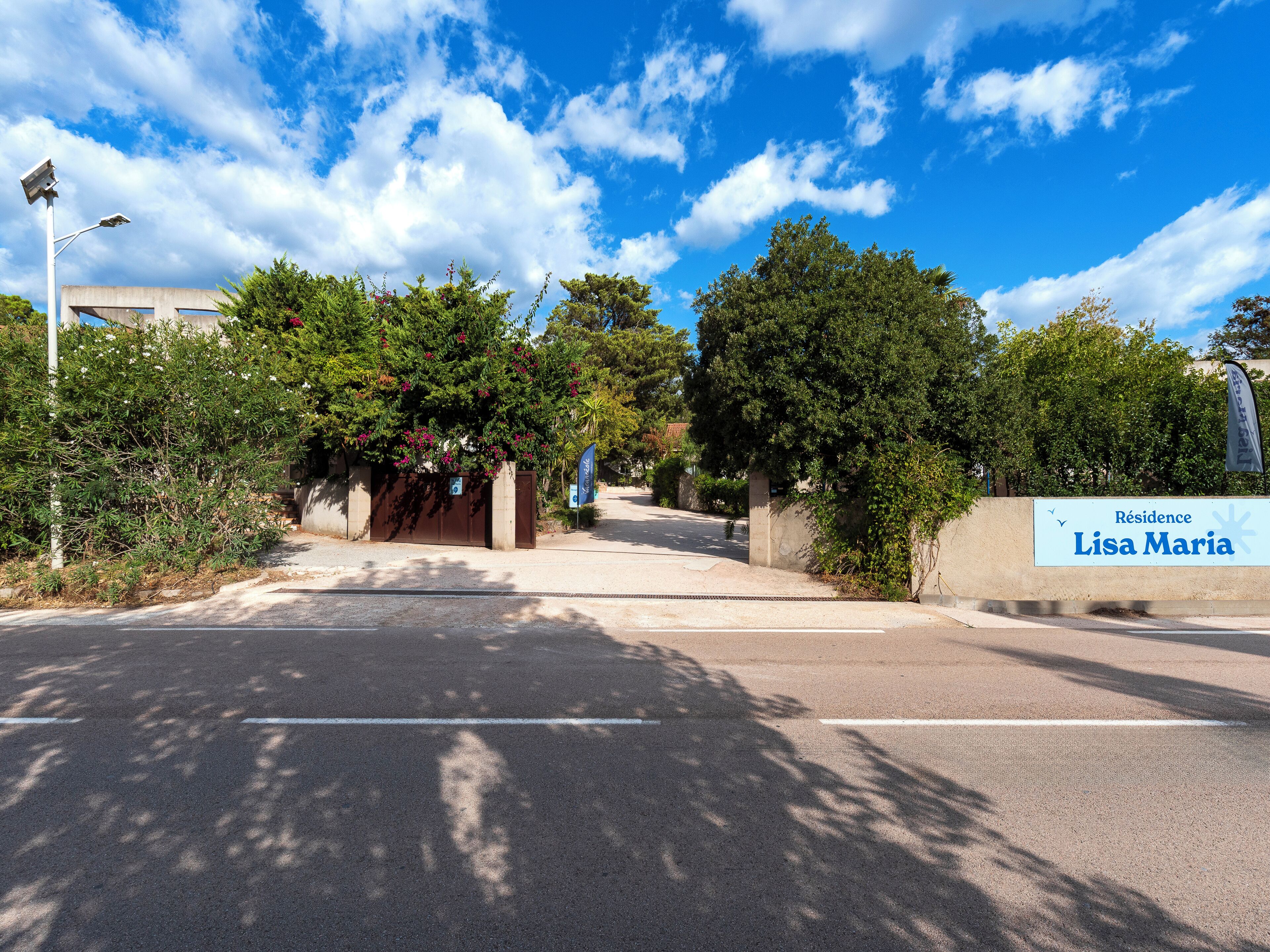 A gated entrance with a sign reading 'Résidence Lisa Maria' and a clear sky above.