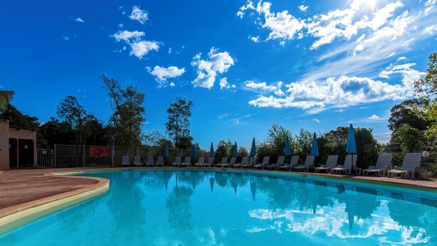 A clear blue swimming pool with lounge chairs and umbrellas, surrounded by trees and a clear sky. - Vacancéole - Résidence Lisa Maria (Sari-Solenzara)