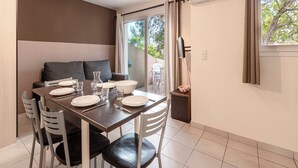 A dining area with a table set for two, a sofa, and a TV mounted on the wall. - Vacancéole - Résidence Lisa Maria (Sari-Solenzara)