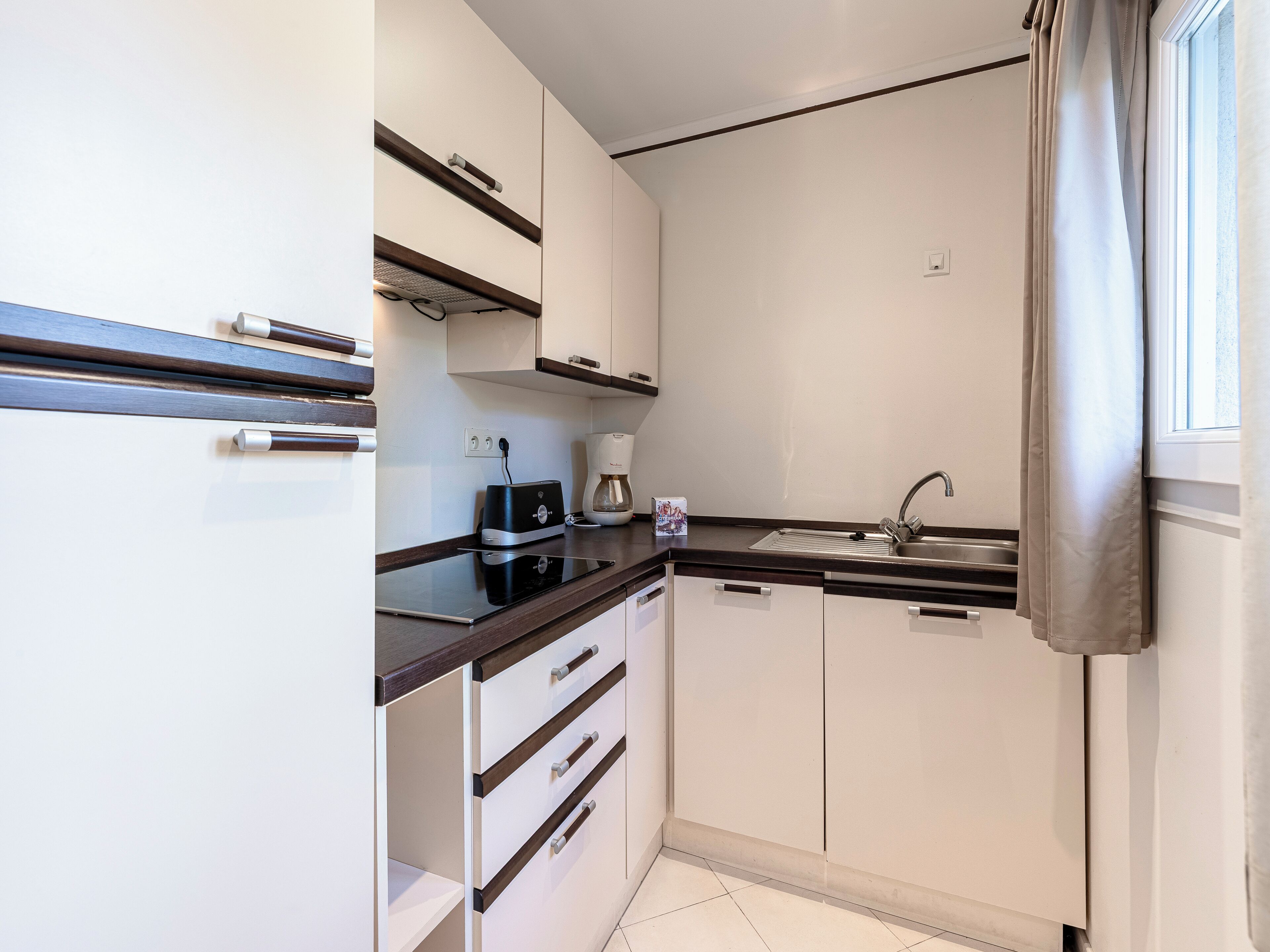 A compact kitchen with white cabinets, a black countertop, and a stainless steel sink.