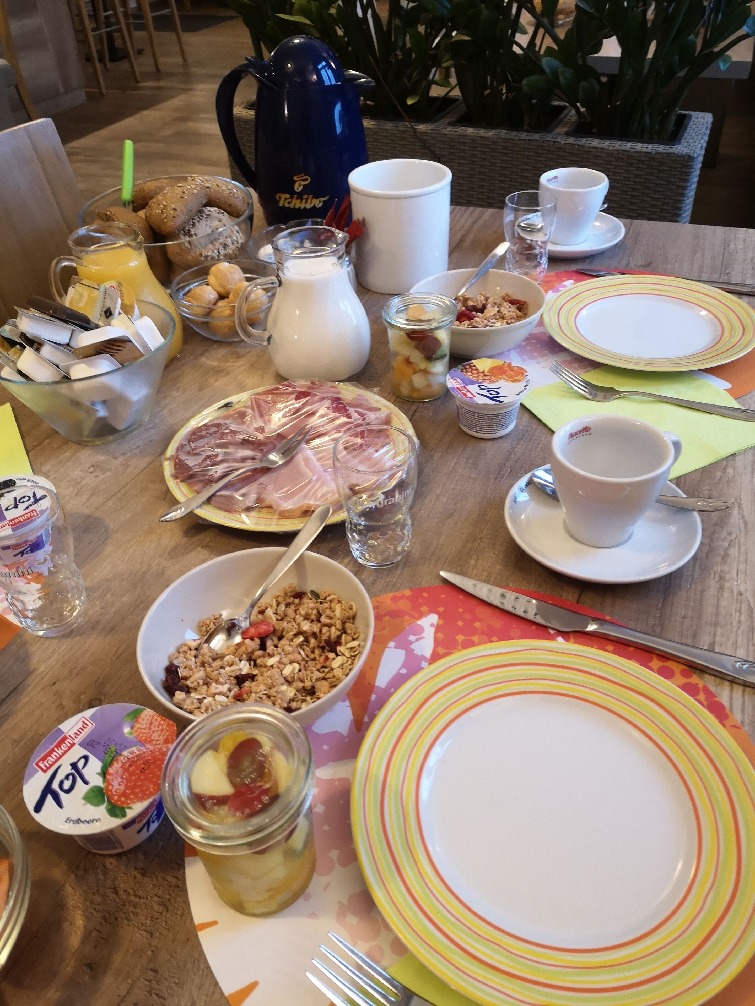 Ein Esstisch mit verschiedenen Speisen, darunter Müsli, Joghurt und einer Fleischplatte.