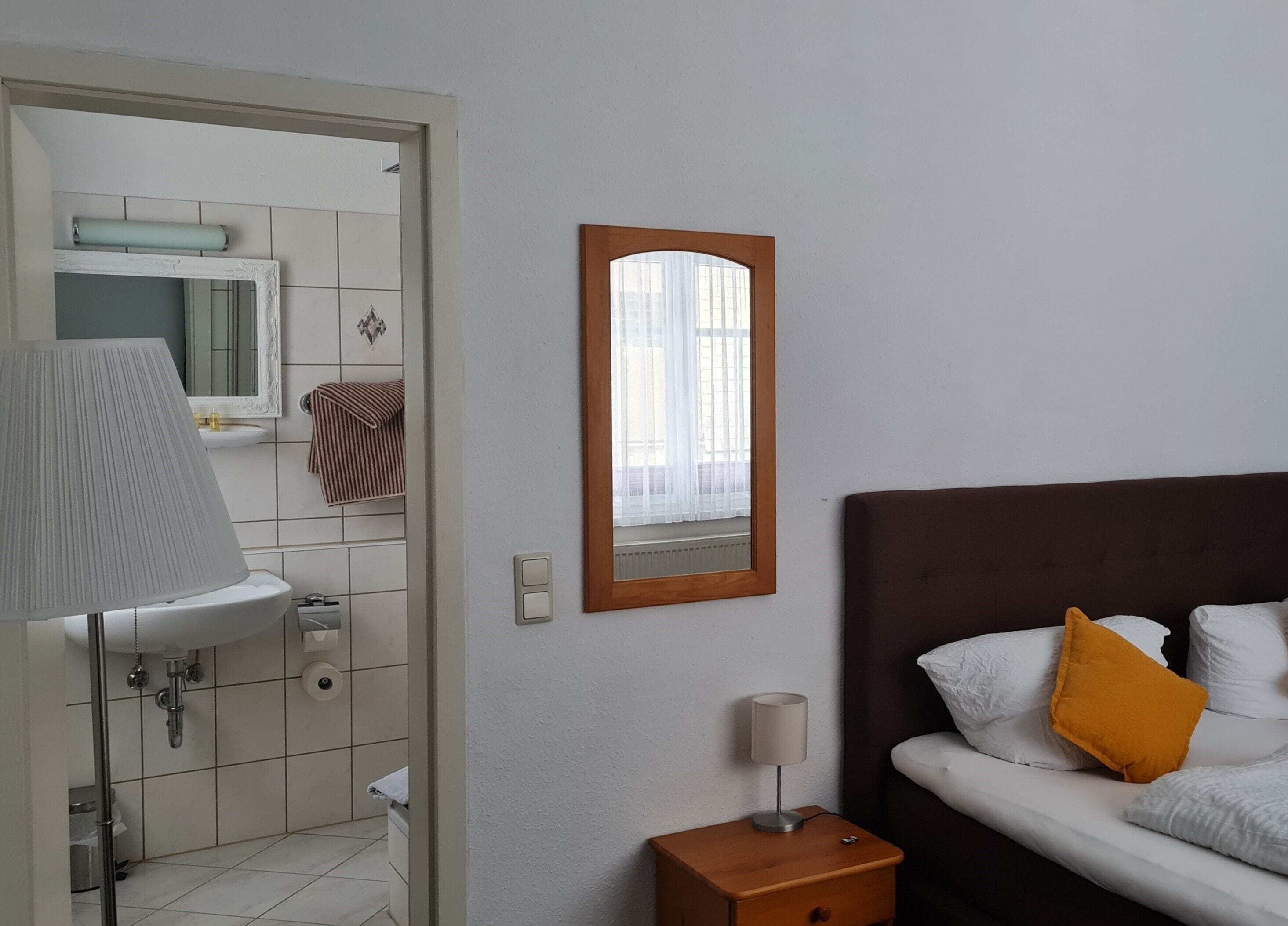 A hotel room with a bed, bedside table, lamp, and a mirror.