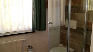 A modern bathroom with a glass shower enclosure, a toilet, and a radiator.