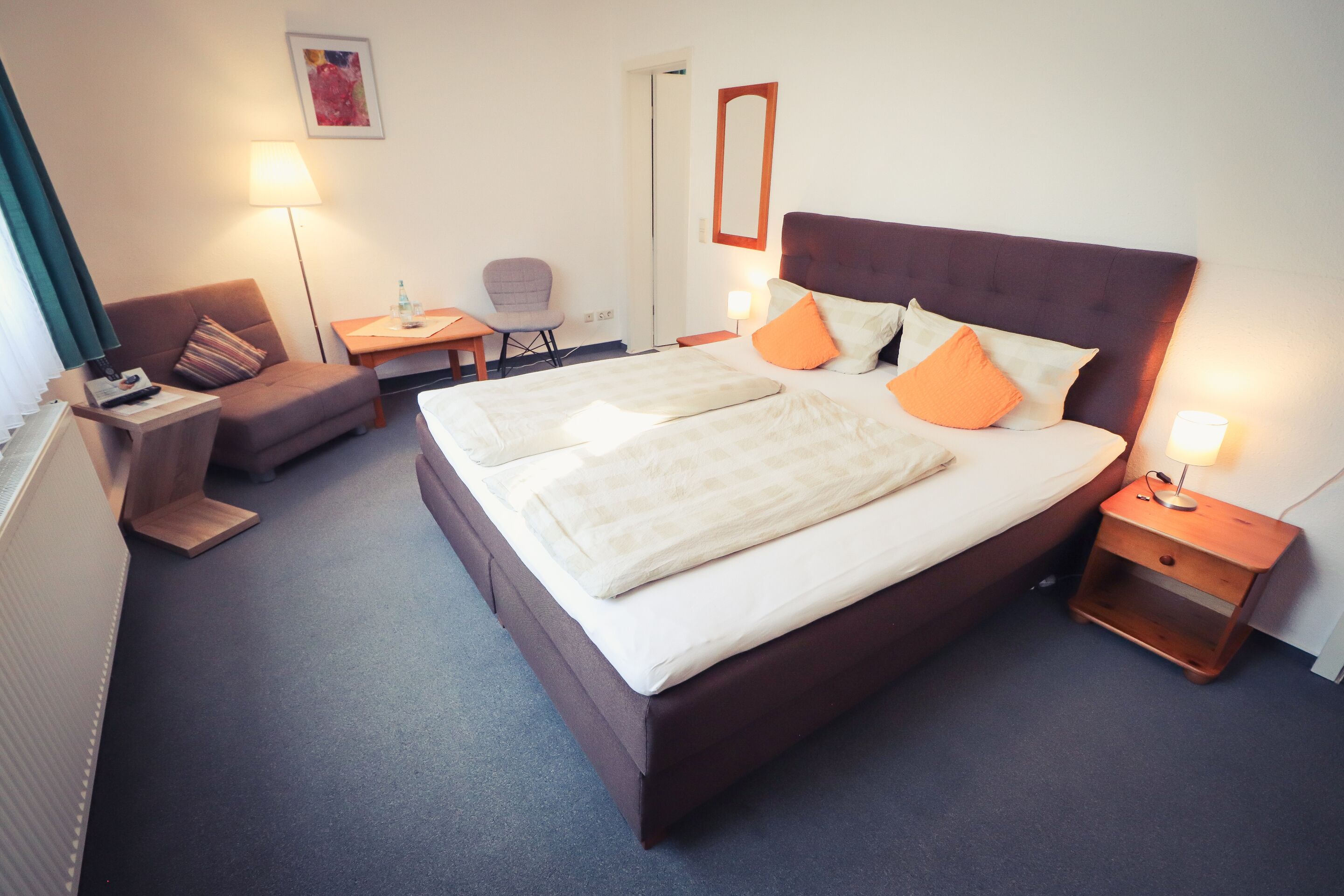 A hotel room with a large bed, two bedside tables, a chair, a desk, and a lamp.
