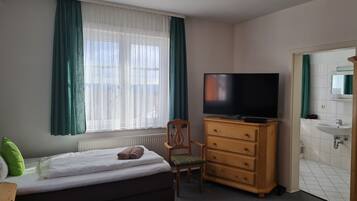 Une chambre à coucher comprenant un lit, une commode en bois, un téléviseur et une salle de bain avec un lavabo et un miroir.