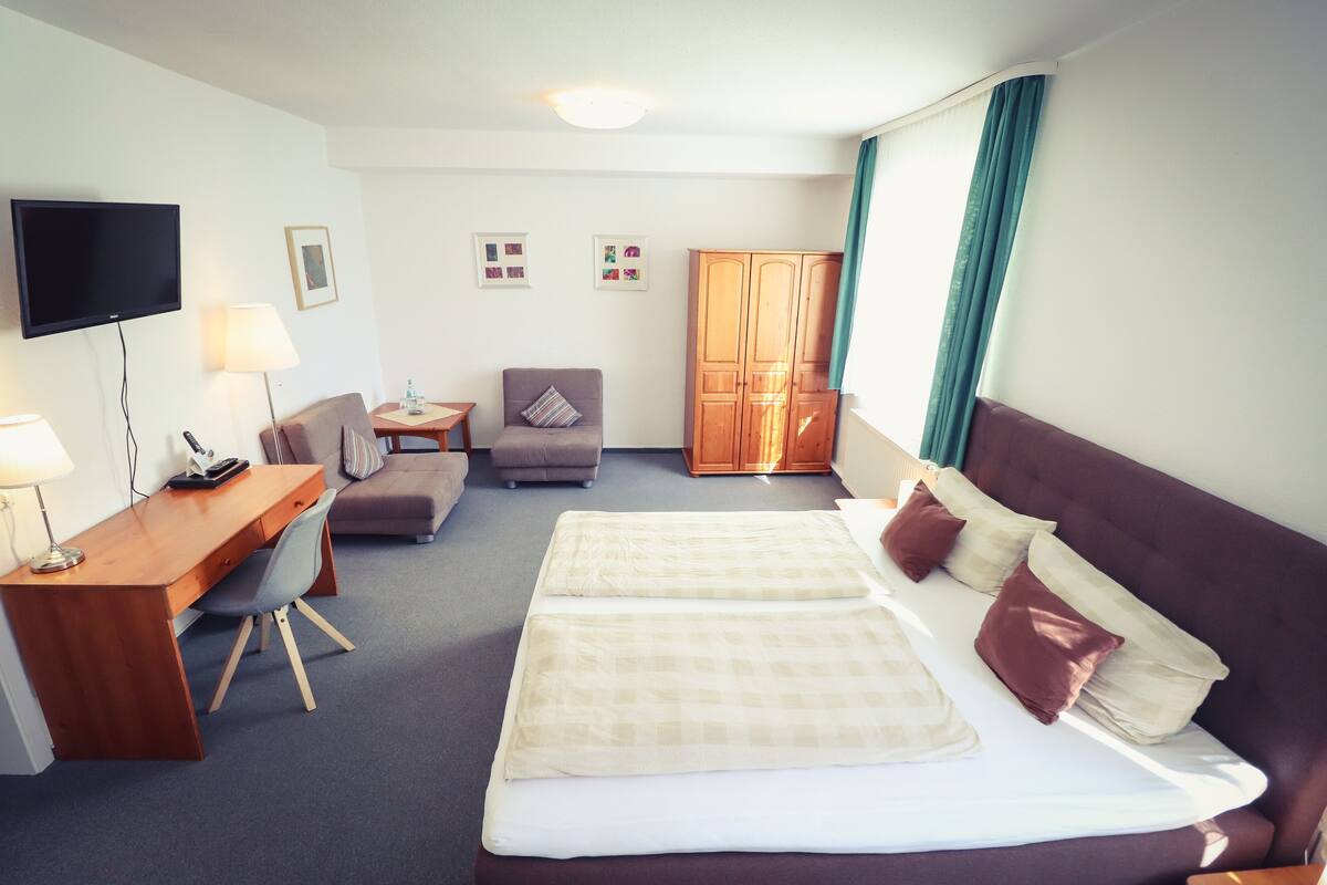 Habitación de hotel con cama, escritorio, silla, televisor y armario.