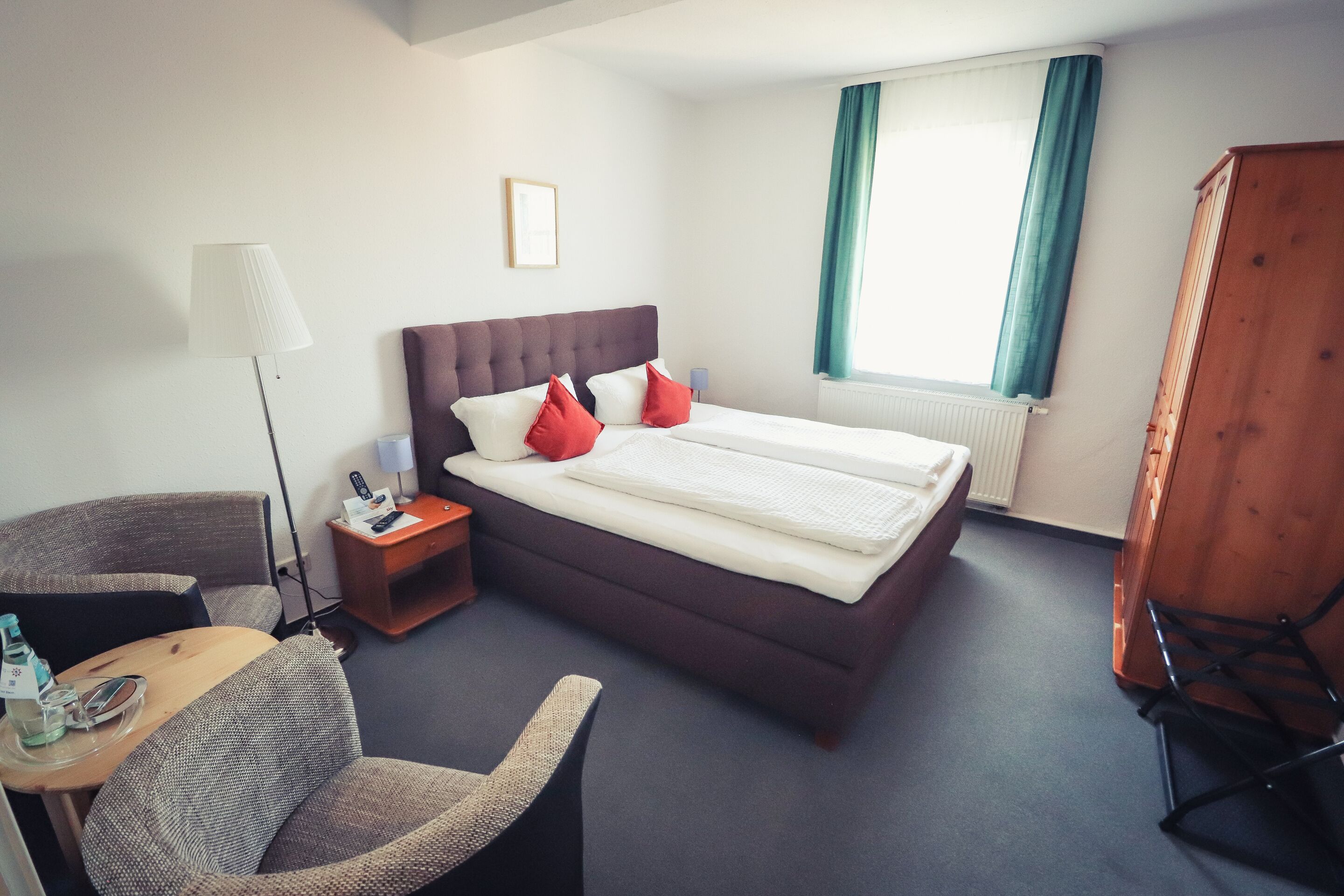 Habitación de hotel con una cama grande, un escritorio con silla, una lámpara y una ventana con cortinas.