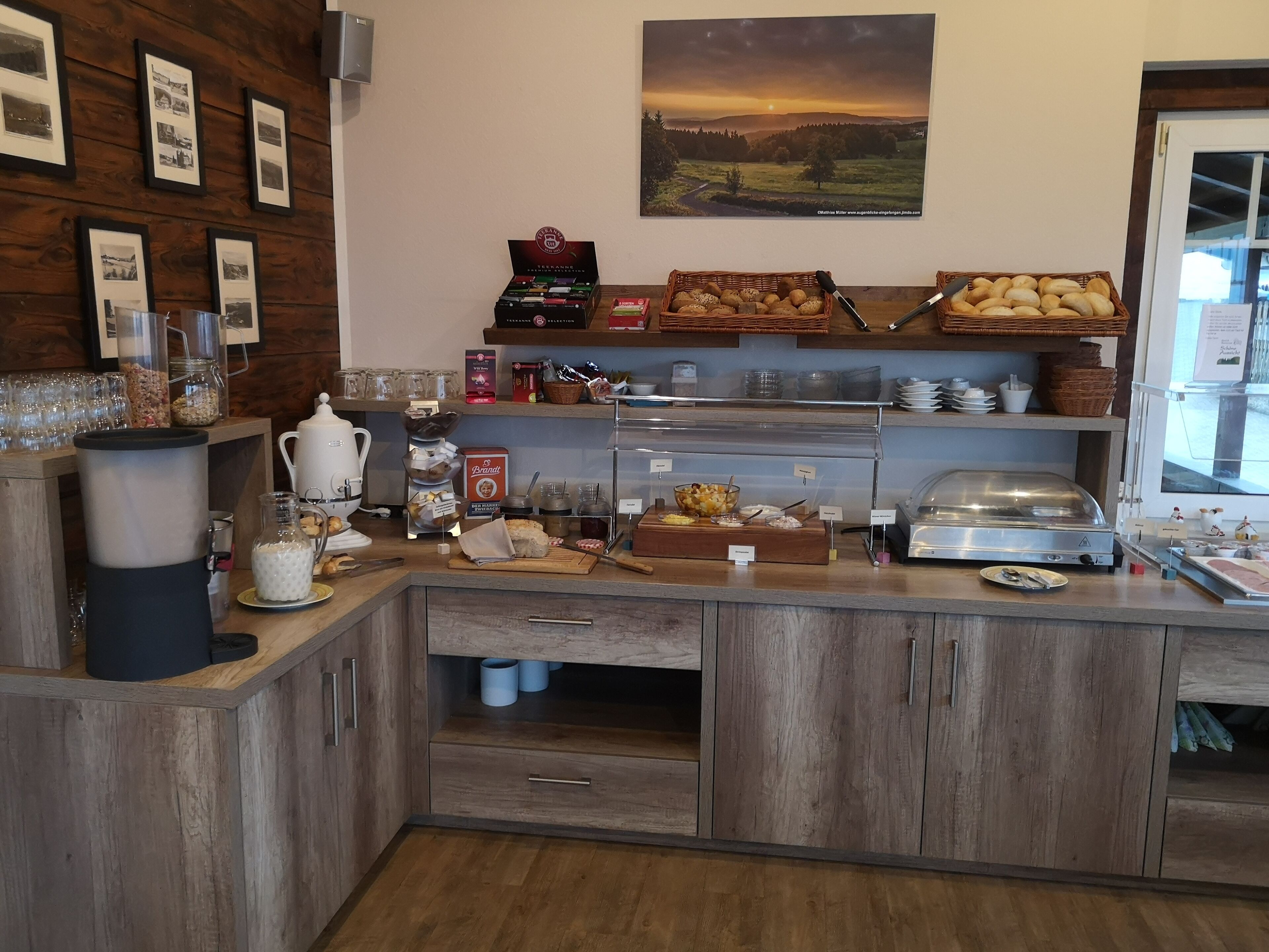 A breakfast buffet with various food items, a coffee station, and a scenic view of a sunset over a landscape.