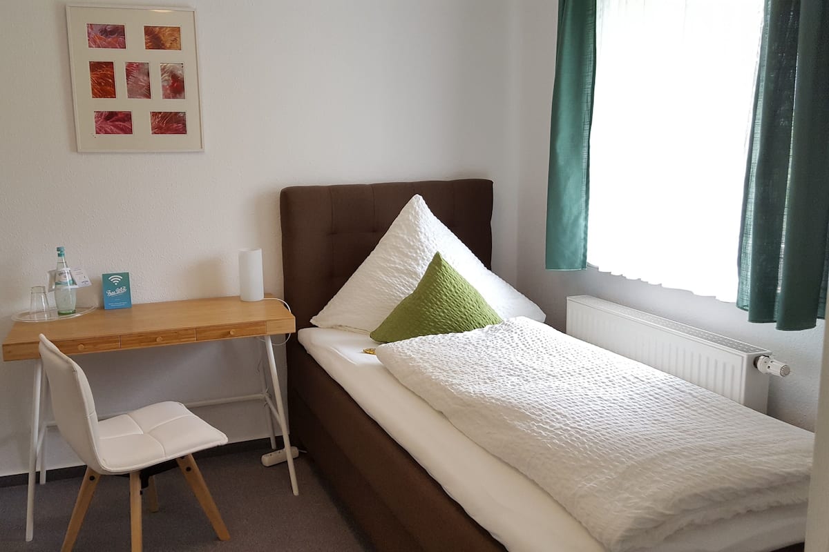 Una habitación pequeña y ordenada con una cama individual, un escritorio y una silla.