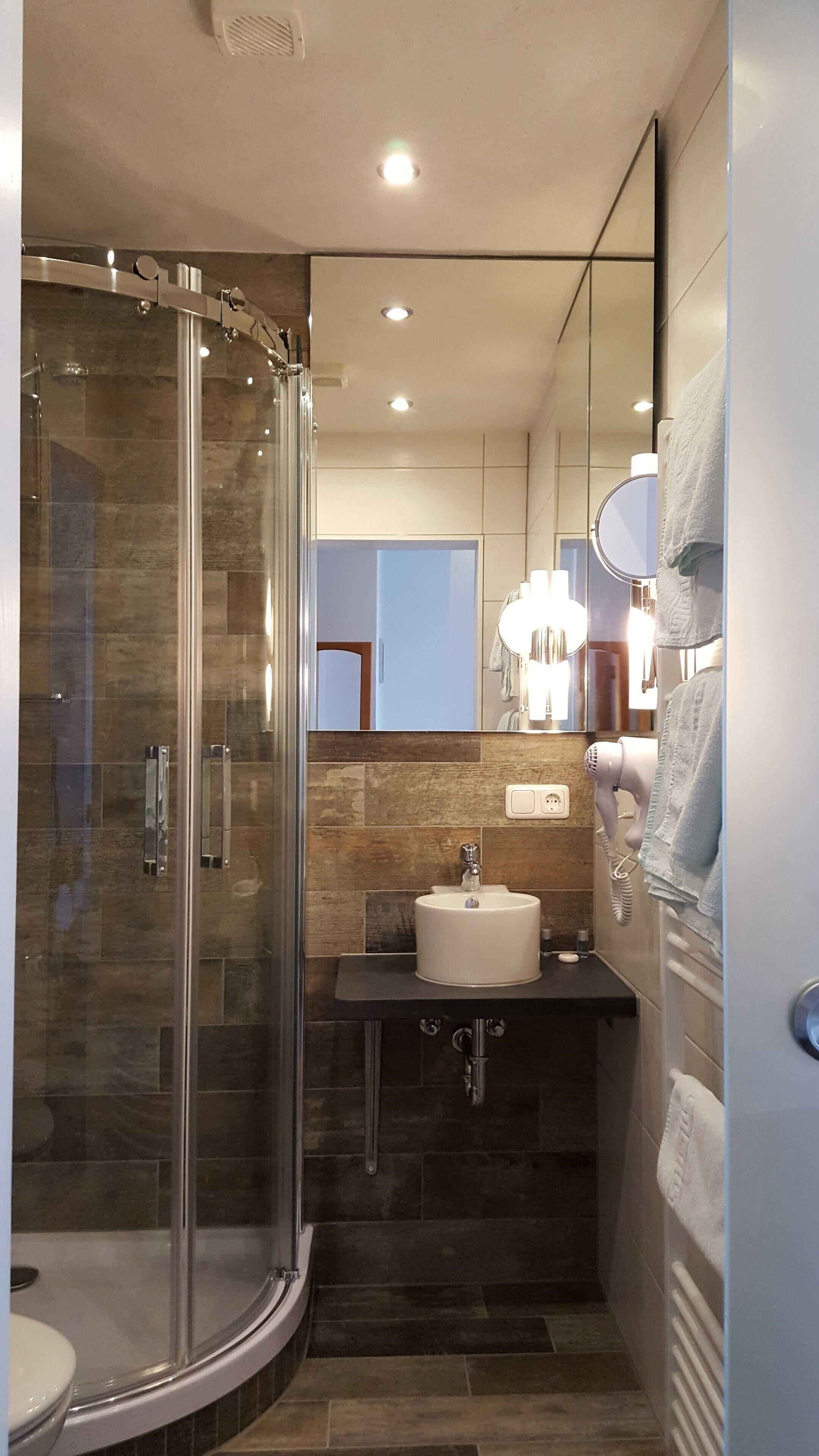 Un baño moderno con ducha de vidrio, un lavamanos con espejo y un perchero para toallas.