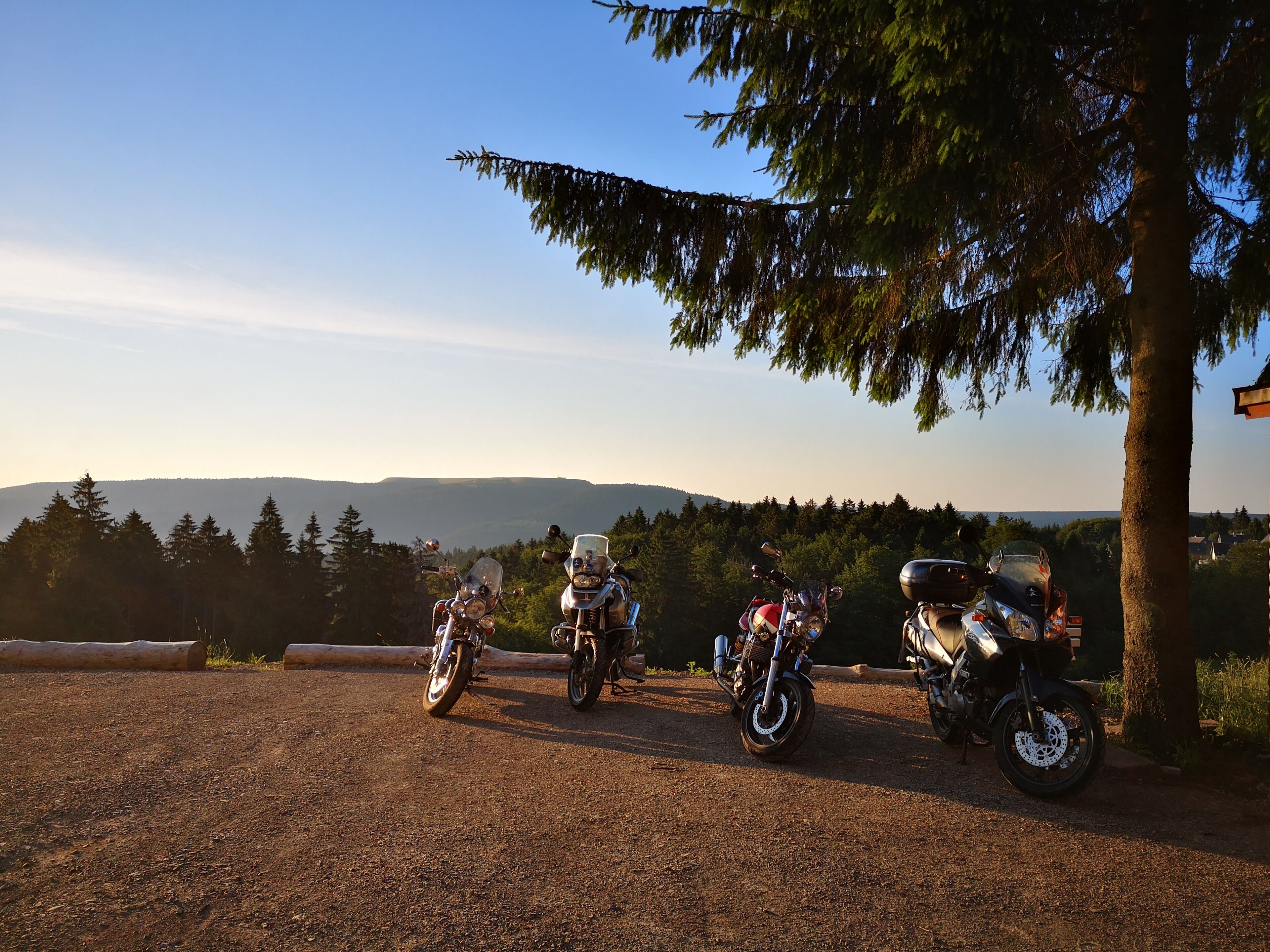 Tres motocicletas estacionadas sobre un camino de grava, con una vista panorámica de colinas y árboles al fondo.