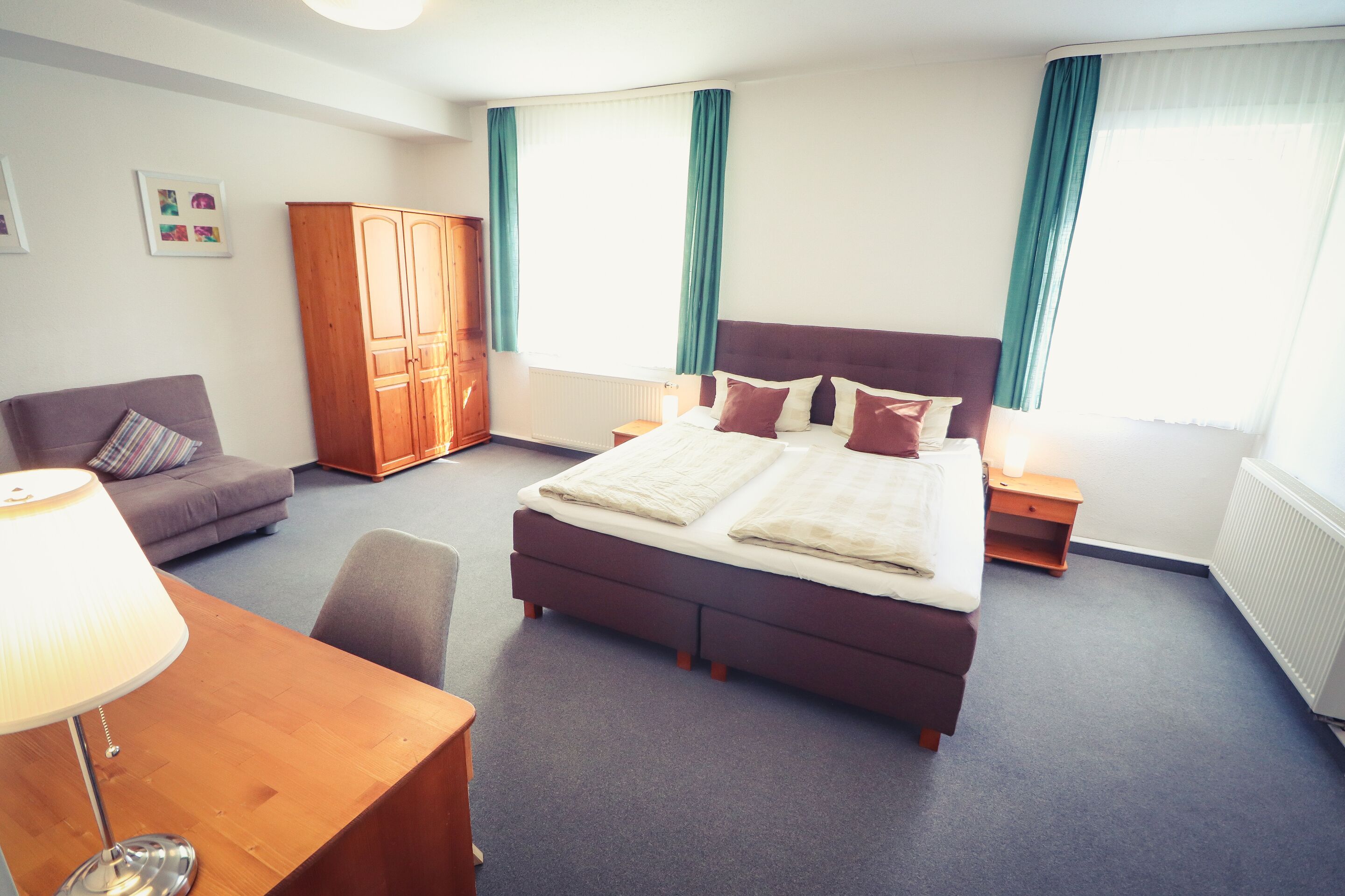 Ein Hotelzimmer mit einem großen Bett, einem Schreibtisch mit Lampe, einem Kleiderschrank und einem Sofa.