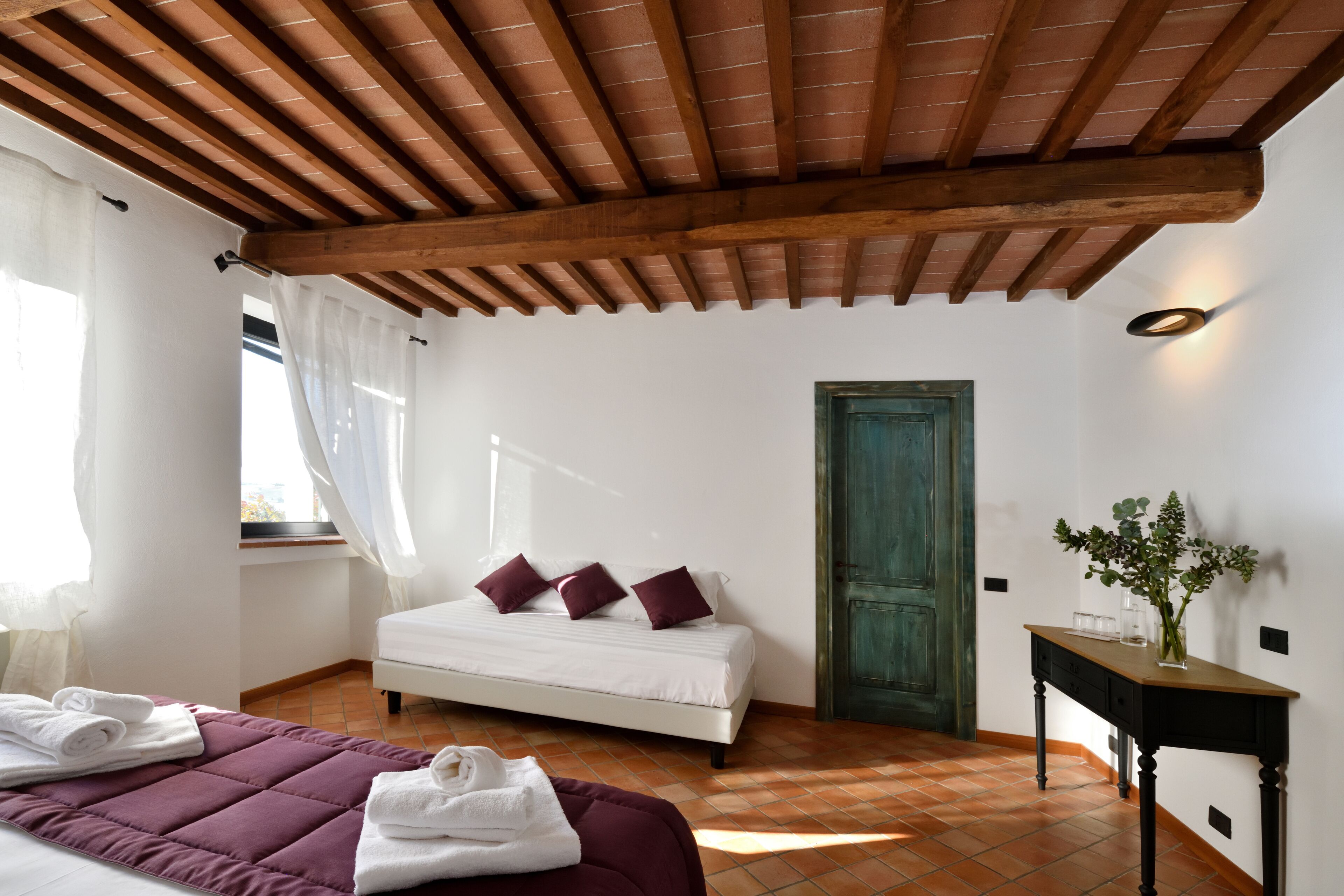 Une chambre à coucher avec un lit, une table de chevet, une fenêtre avec des rideaux, un plafond en bois et une porte verte.