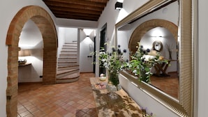 A hallway with tiled flooring, brick arches, a wooden ceiling, and a mirror with a decorative frame. - Porsenna Resort (Castiglione del Lago)