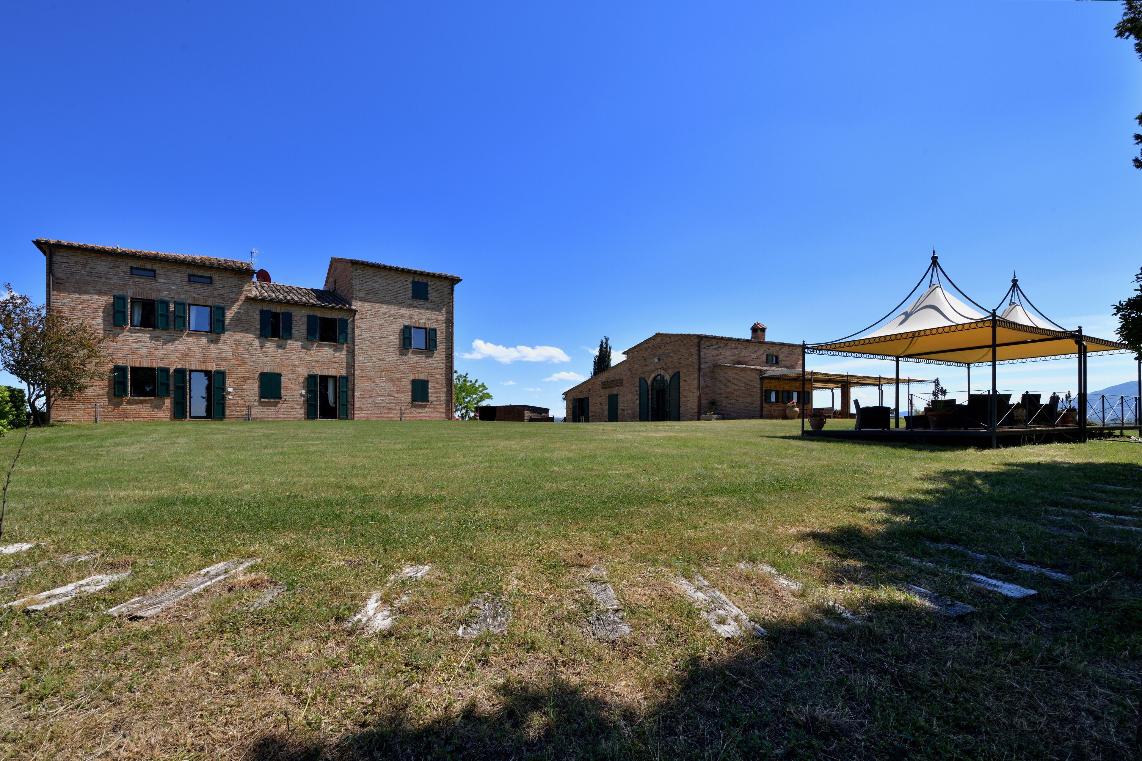 A large brick building with multiple windows and doors, a covered outdoor seating area, and a clear blue sky.