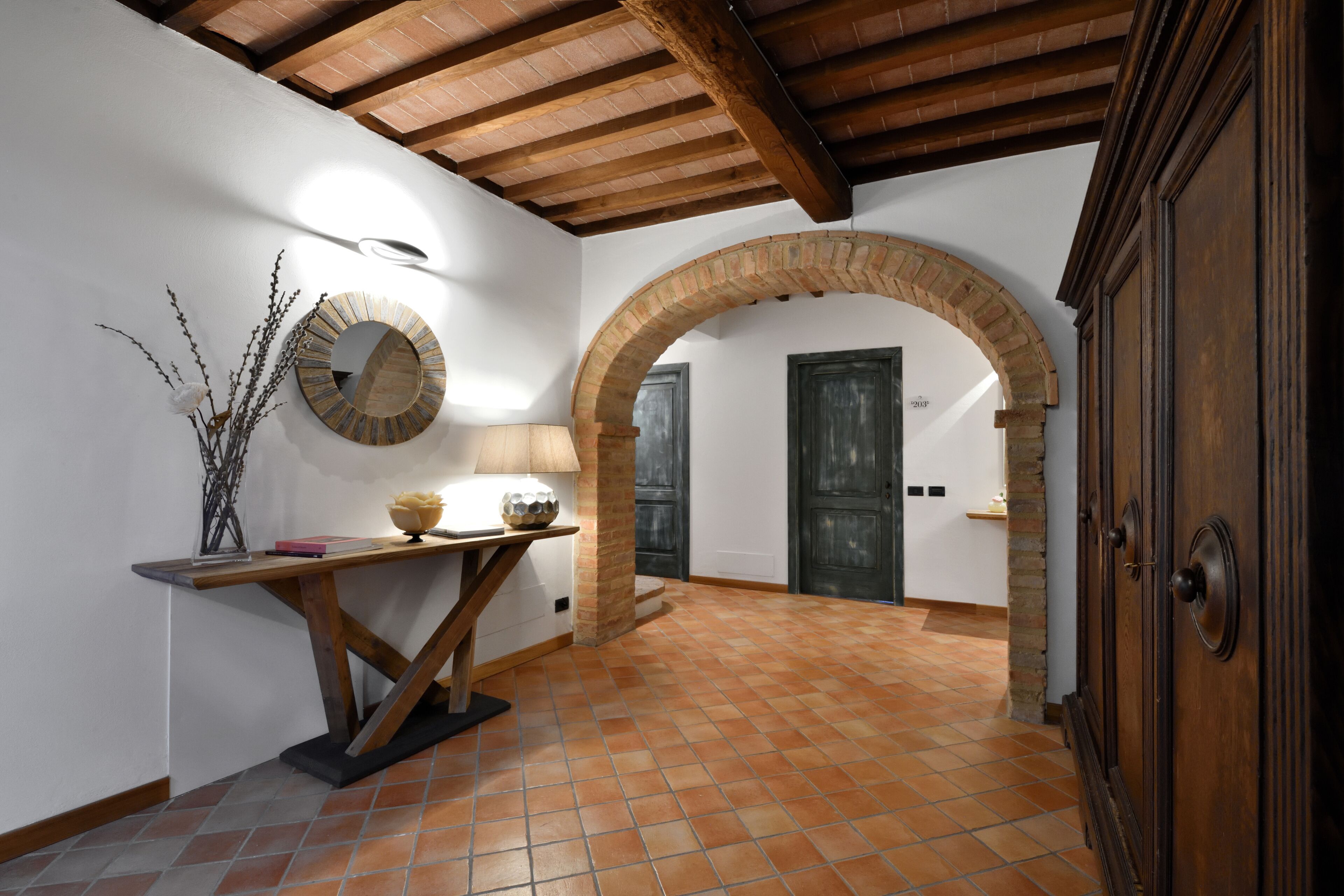 Una habitación con suelo de baldosas, una mesa de madera con lámpara, un espejo y una puerta con arco.