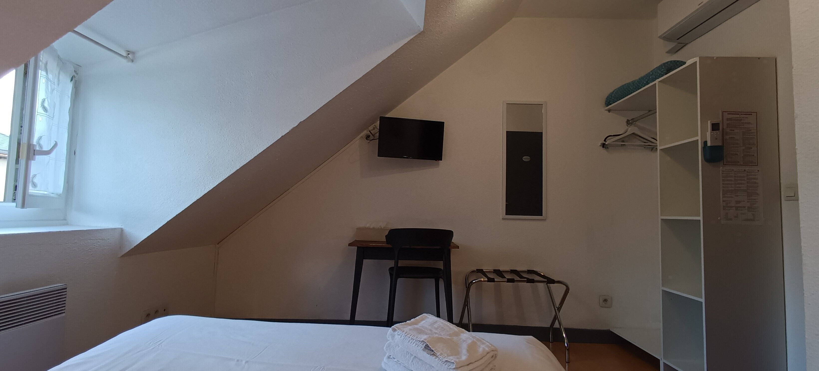 Un dormitorio con cama, una silla, televisor, armario y ventana.