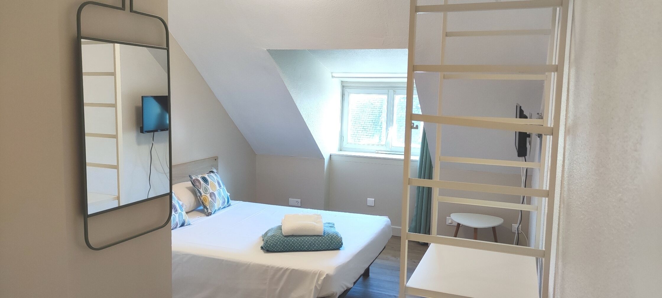Een slaapkamer met een bed, een spiegel, een raam en een klein tafeltje.