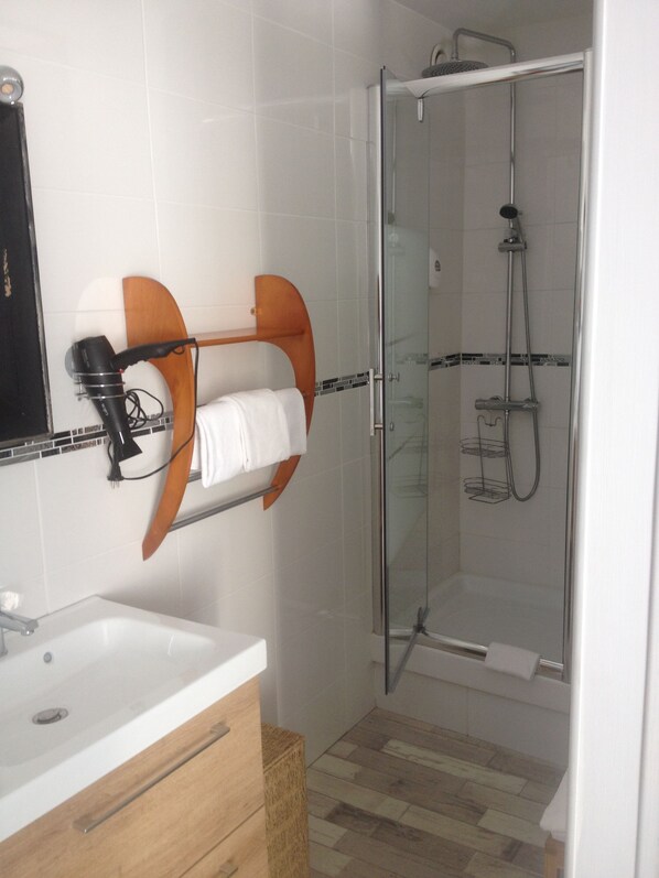 Un baño moderno con ducha de vidrio, lavamanos blanco y toallero con estante de madera.