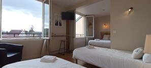 Habitación de hotel con dos camas, televisión, balcón y vistas al exterior.