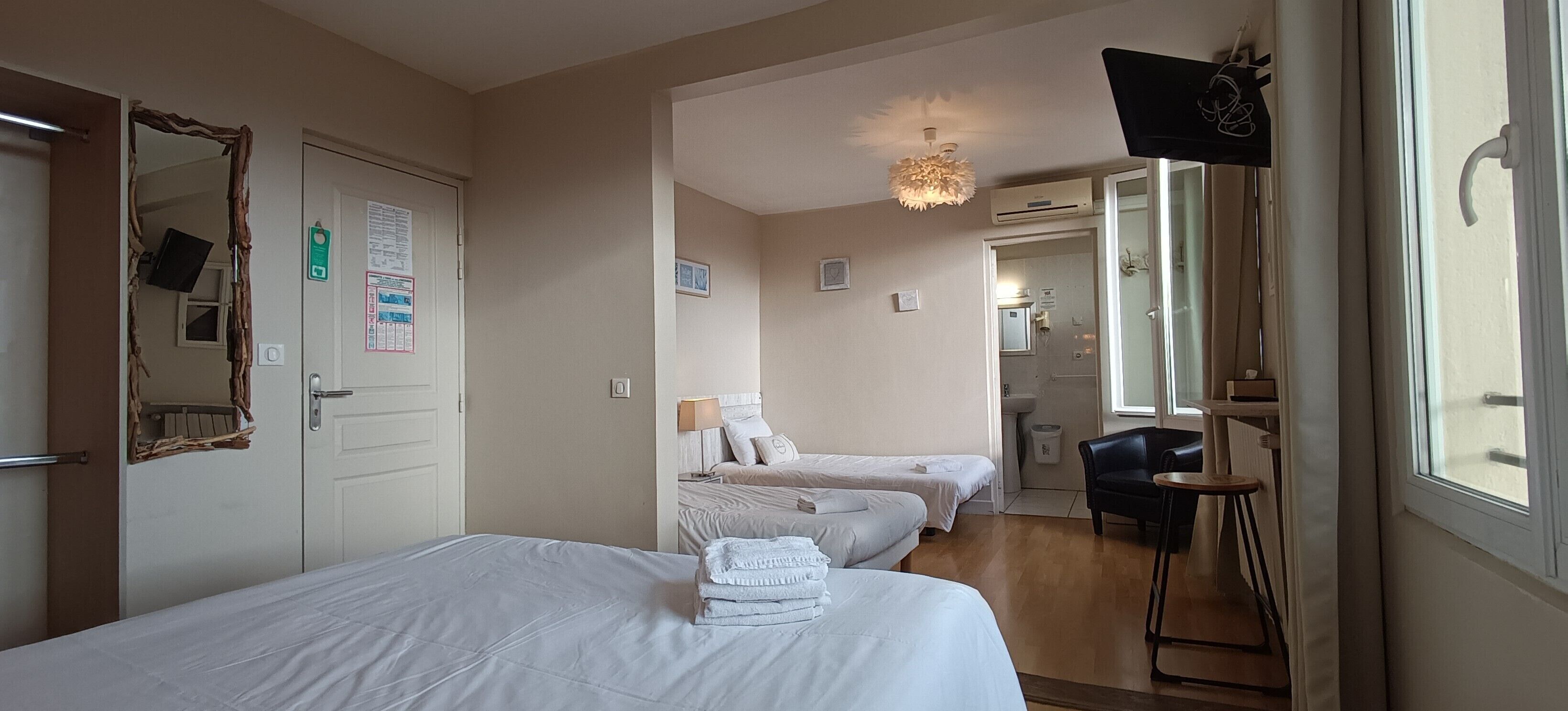 Een hotelkamer met twee bedden, een spiegel, een plafondlamp, een raam en een klein tafeltje.
