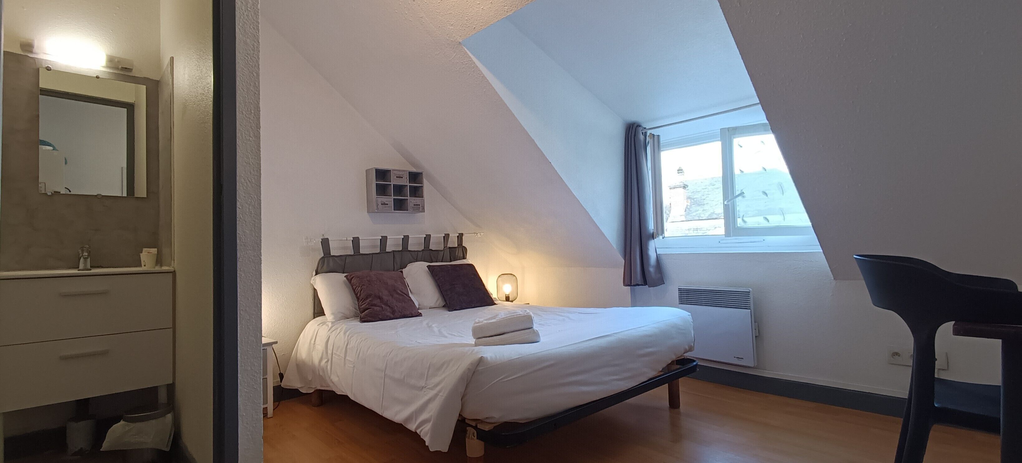 A bedroom with a bed, a bedside table, a mirror, a window, and a radiator.