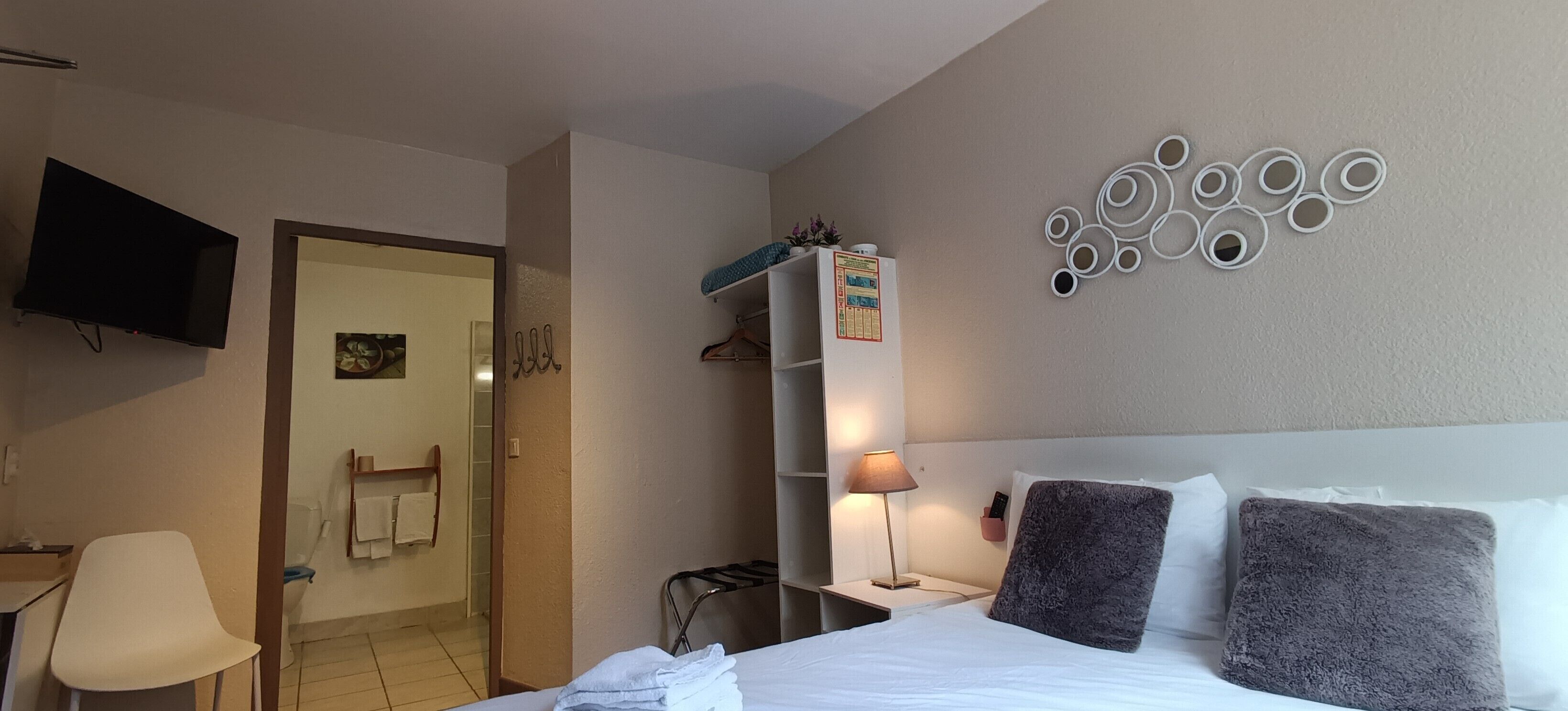 A hotel room with a bed, a TV, a desk, a chair, a bathroom, and a wall decoration.