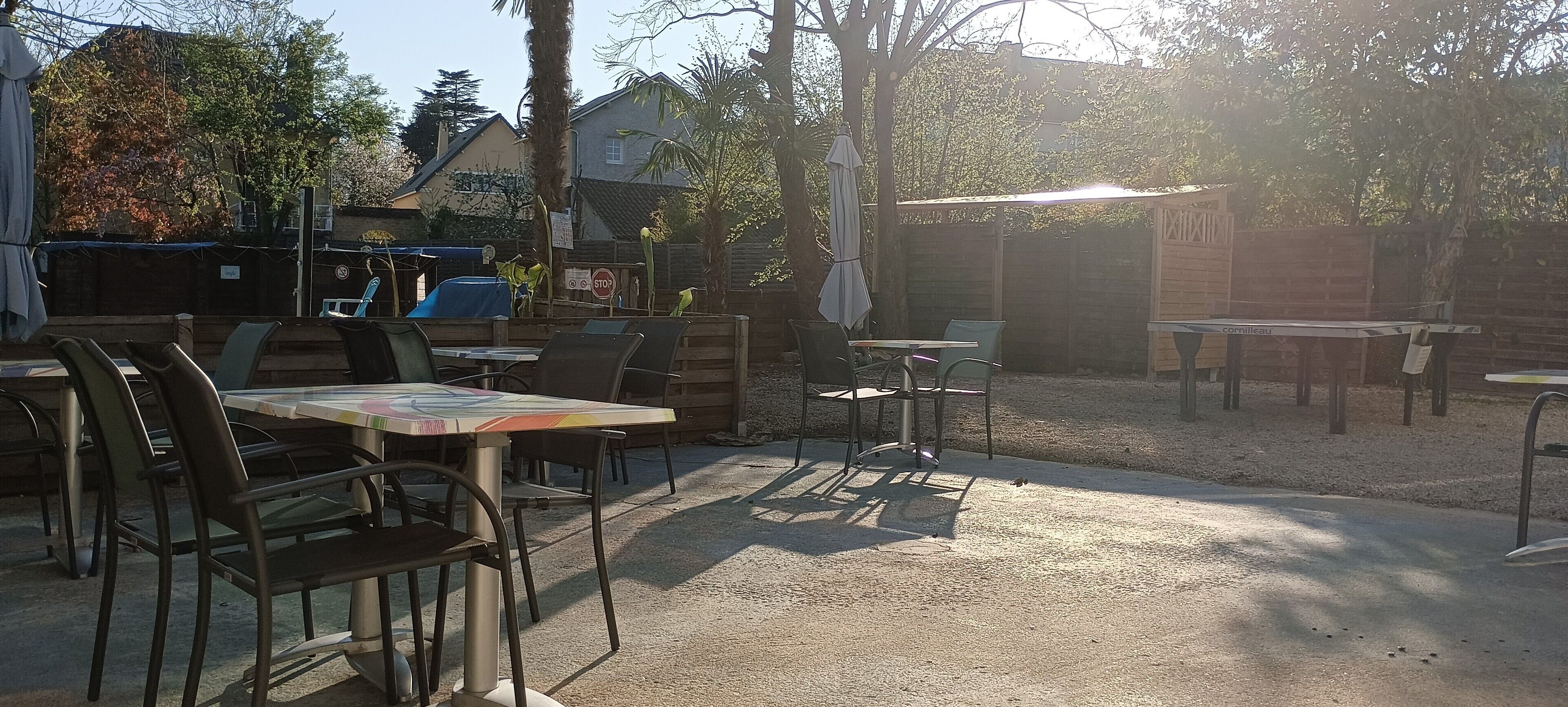 An outdoor seating area with tables and chairs, surrounded by trees and a fence.