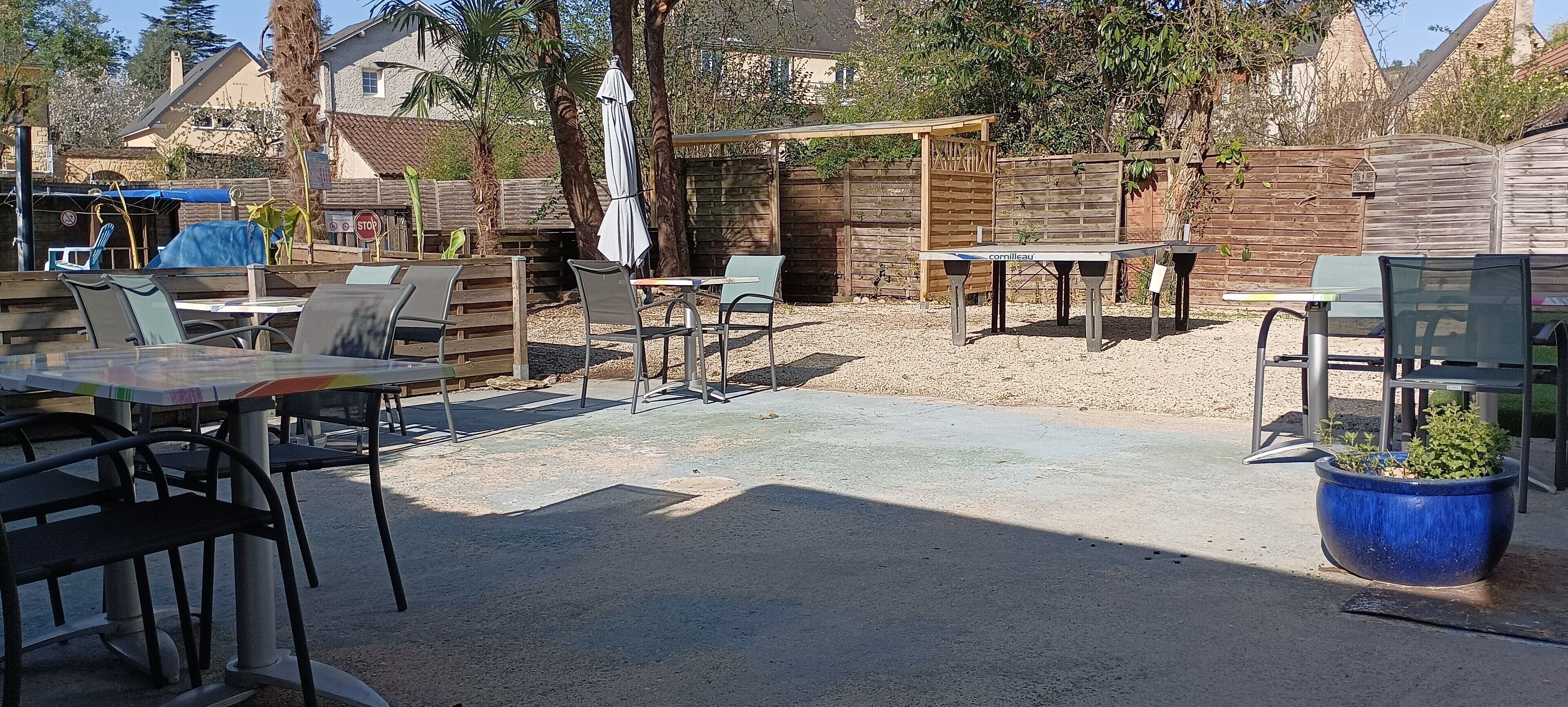 Un patio al aire libre con mesas y sillas, una zona de estar techada y una valla de madera.