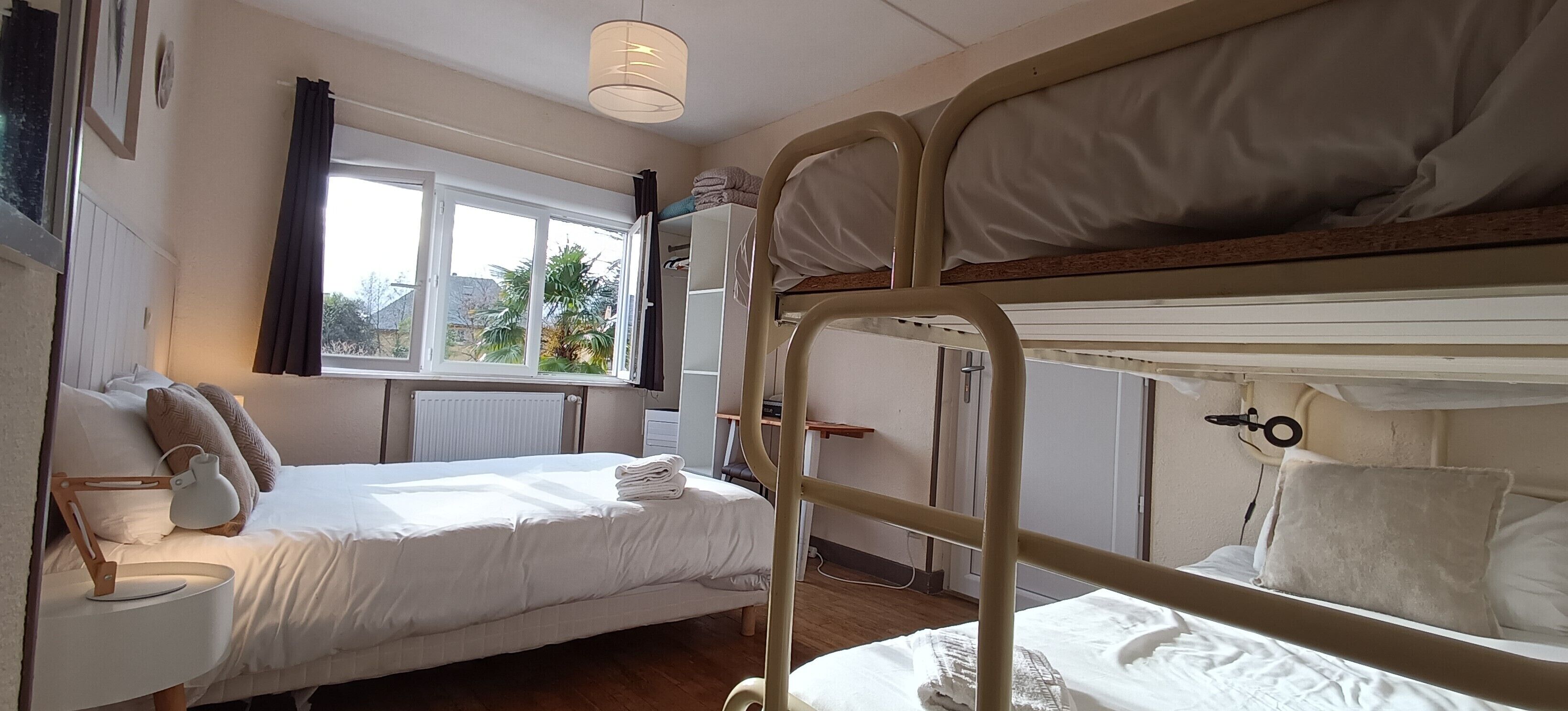 A bunk bed room with a window, a bedside table with a lamp, and a radiator.
