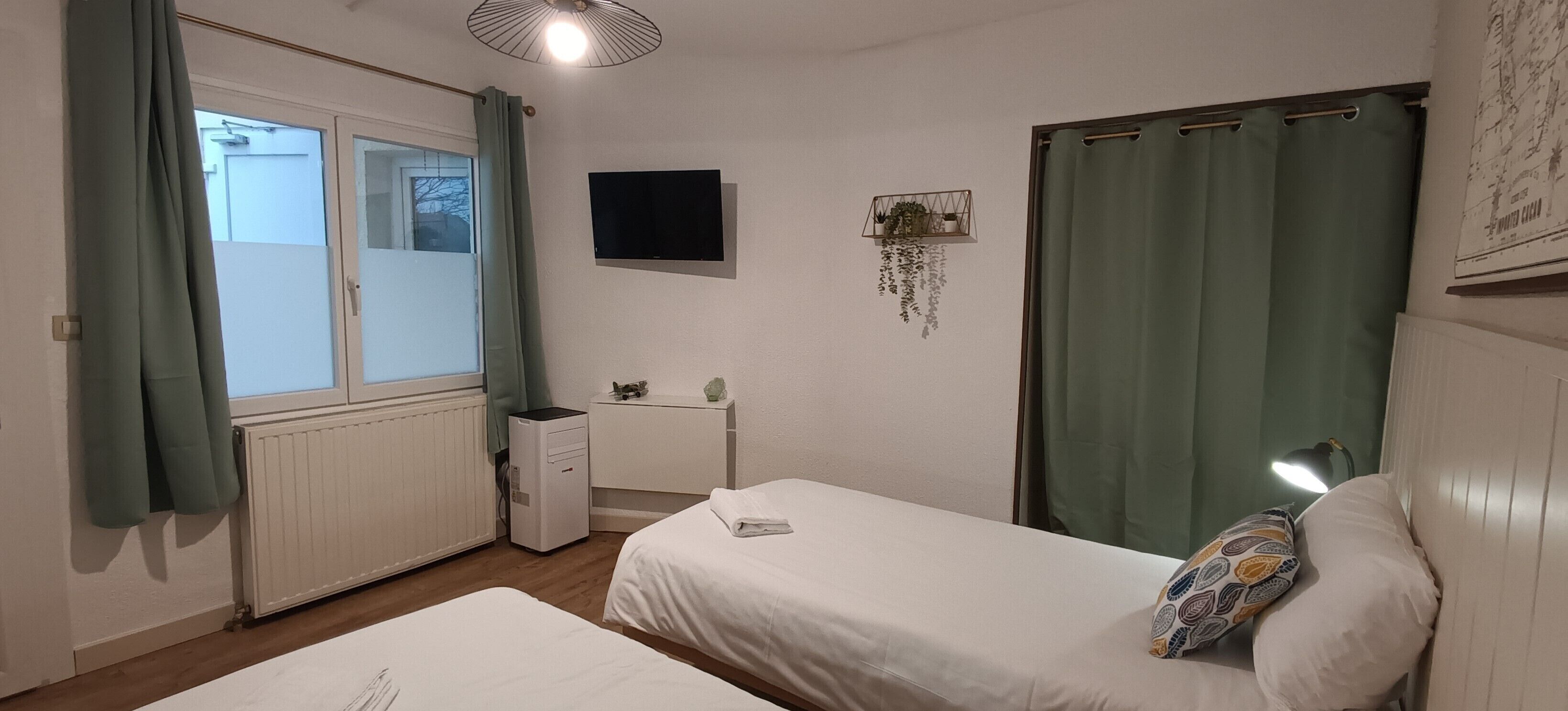 A bedroom with two beds, a radiator, a desk, a TV, and a window with curtains.