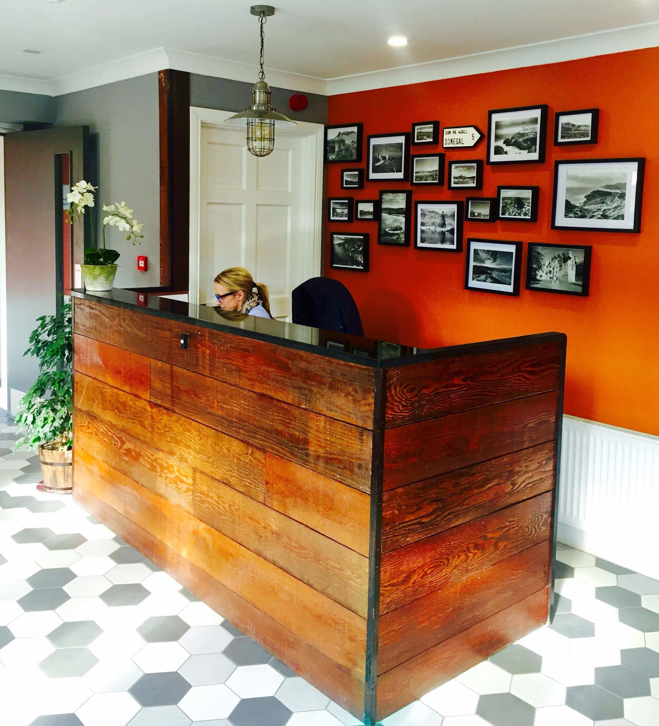 A reception desk with a wooden finish, a potted plant, and a wall with framed photographs.