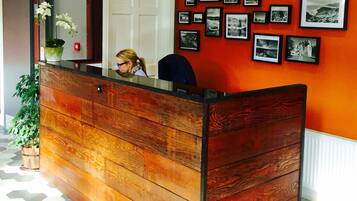A reception desk with a wooden finish, a potted plant, and a wall with framed photographs.
