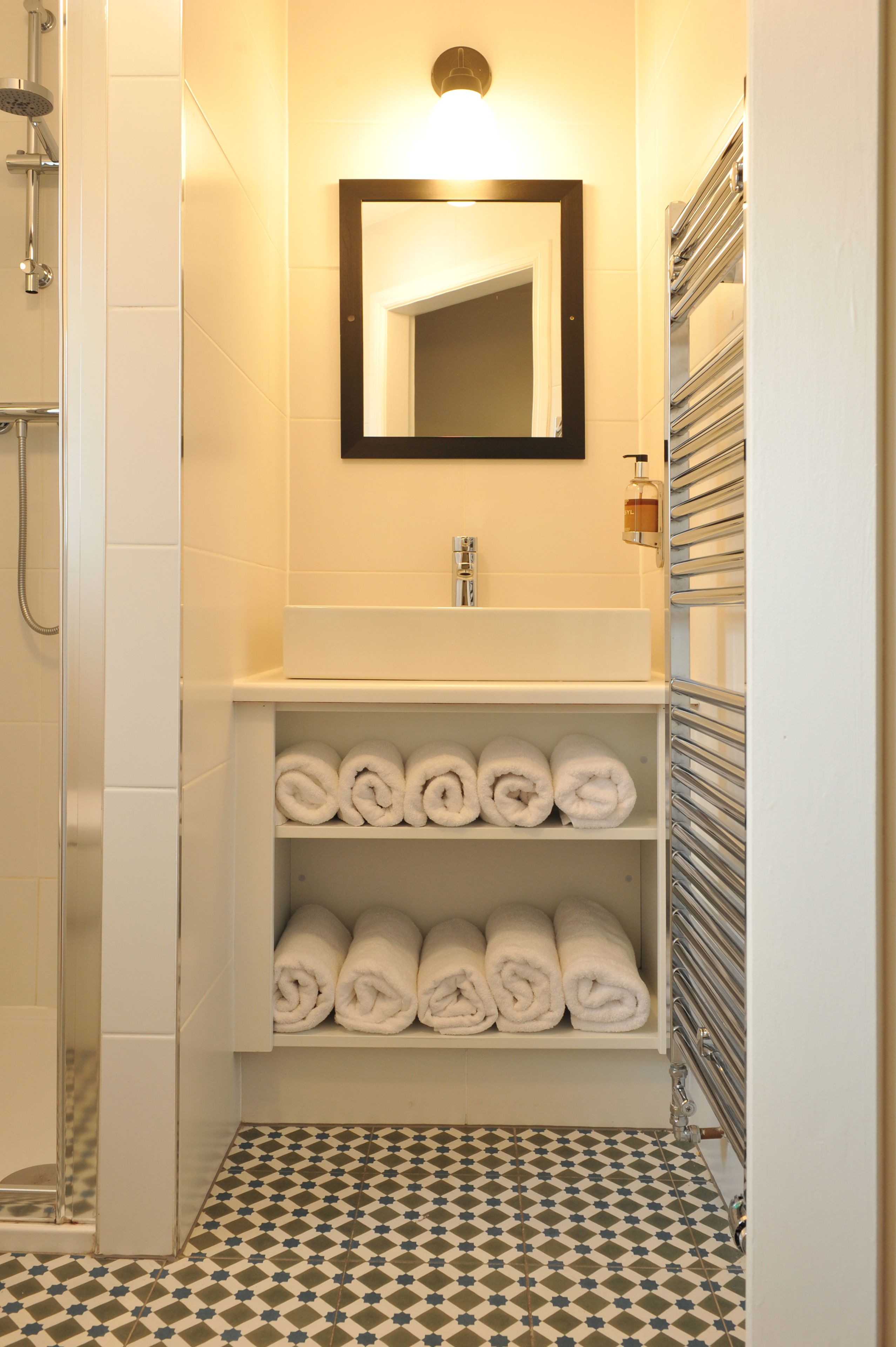 Een badkamer met een douche, wastafel, spiegel en planken met opgerolde handdoeken.