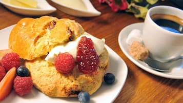 A plate with a scone, raspberries, and blueberries, accompanied by a cup of coffee and a small dish of butter.