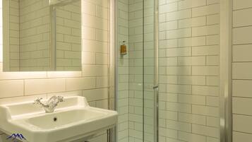 Une salle de bain avec un lavabo blanc, une cabine de douche en verre et des murs recouverts de carreaux blancs.