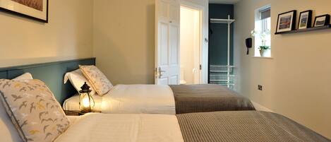 A hotel room with two beds, a nightstand with a lamp, a door leading to a balcony, and a window with a plant.