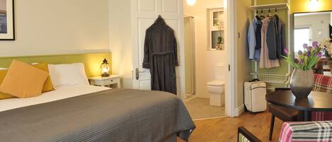 A hotel room with a bed, bedside table, lamp, and a bathroom with a shower and toilet.