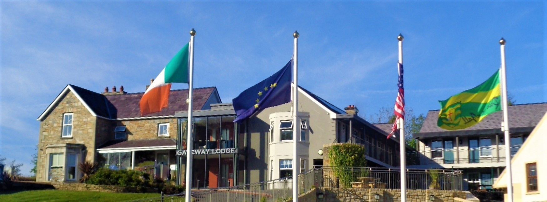 A building with a stone facade, a sign reading "Gateway Lodge," and flags of Ireland, the EU, the USA, and Brazil.