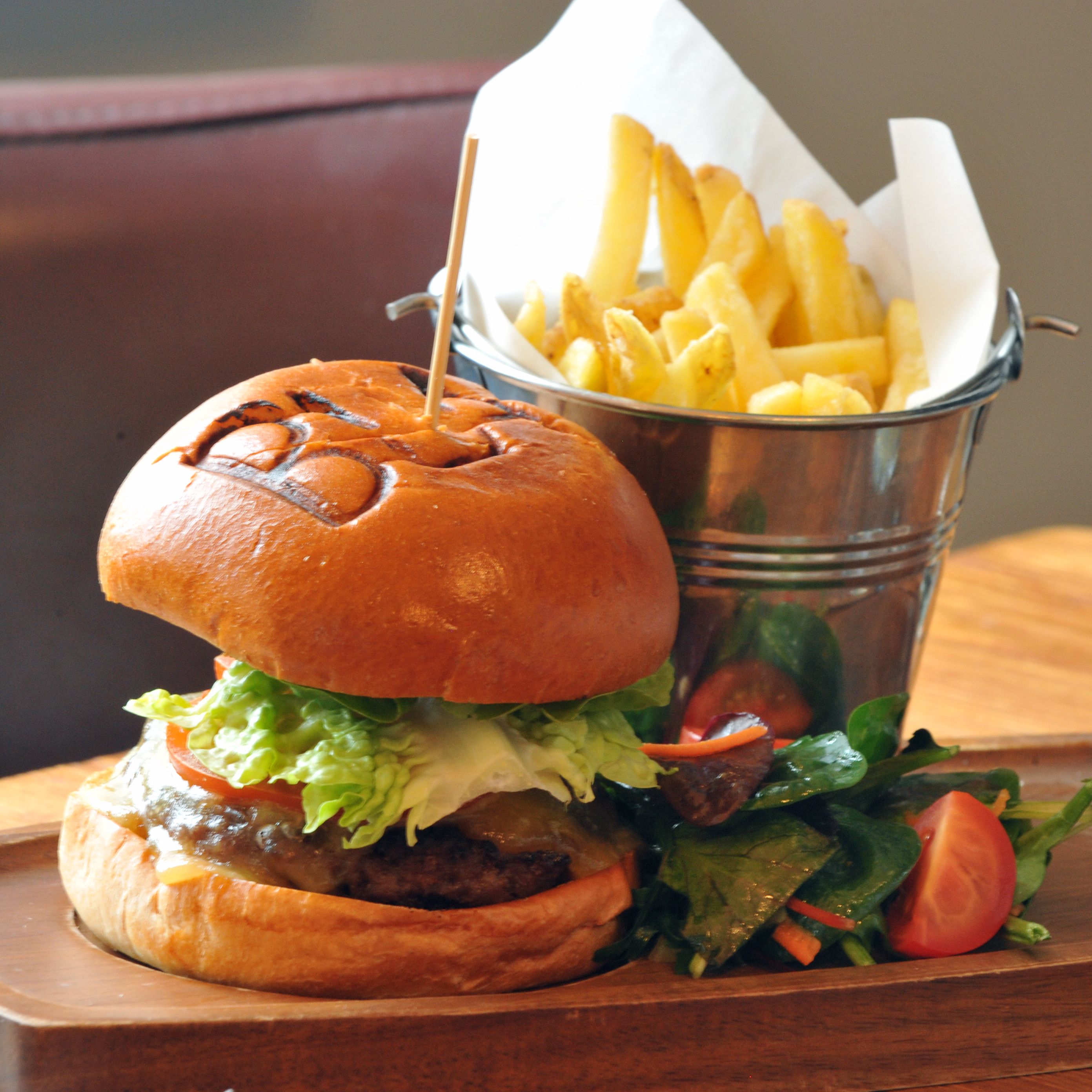 A burger with fries and salad on a wooden table.