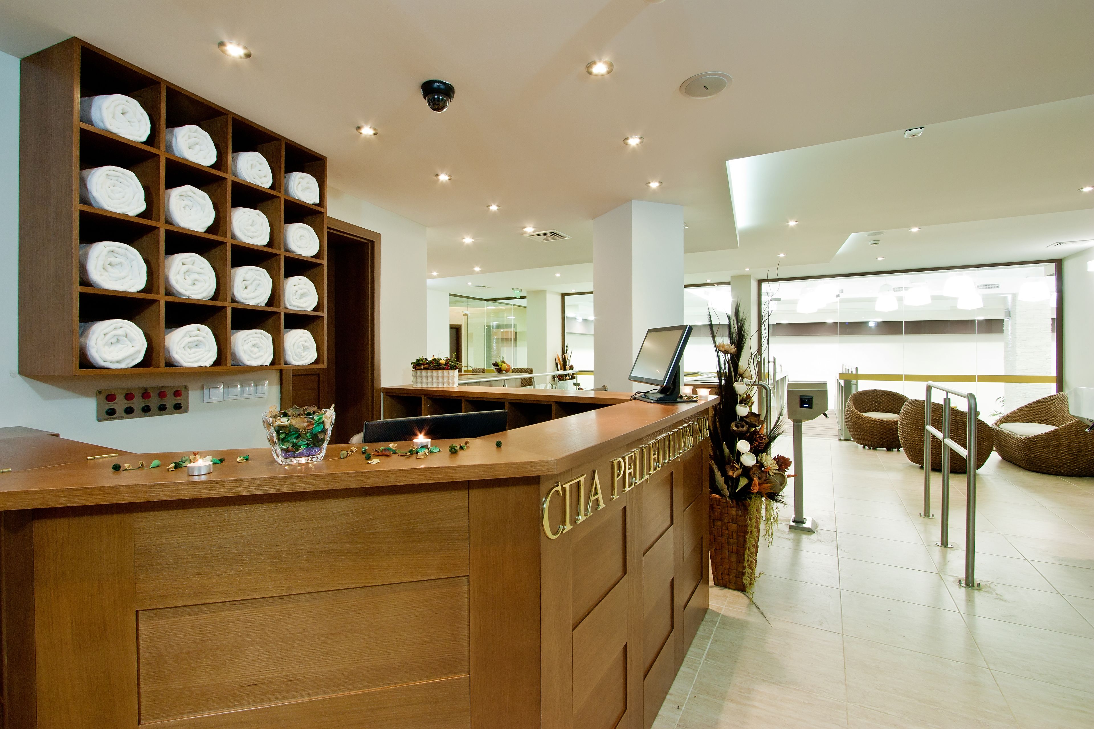 A hotel reception area with a wooden reception desk, a wall-mounted control panel, and a seating area with wicker chairs.