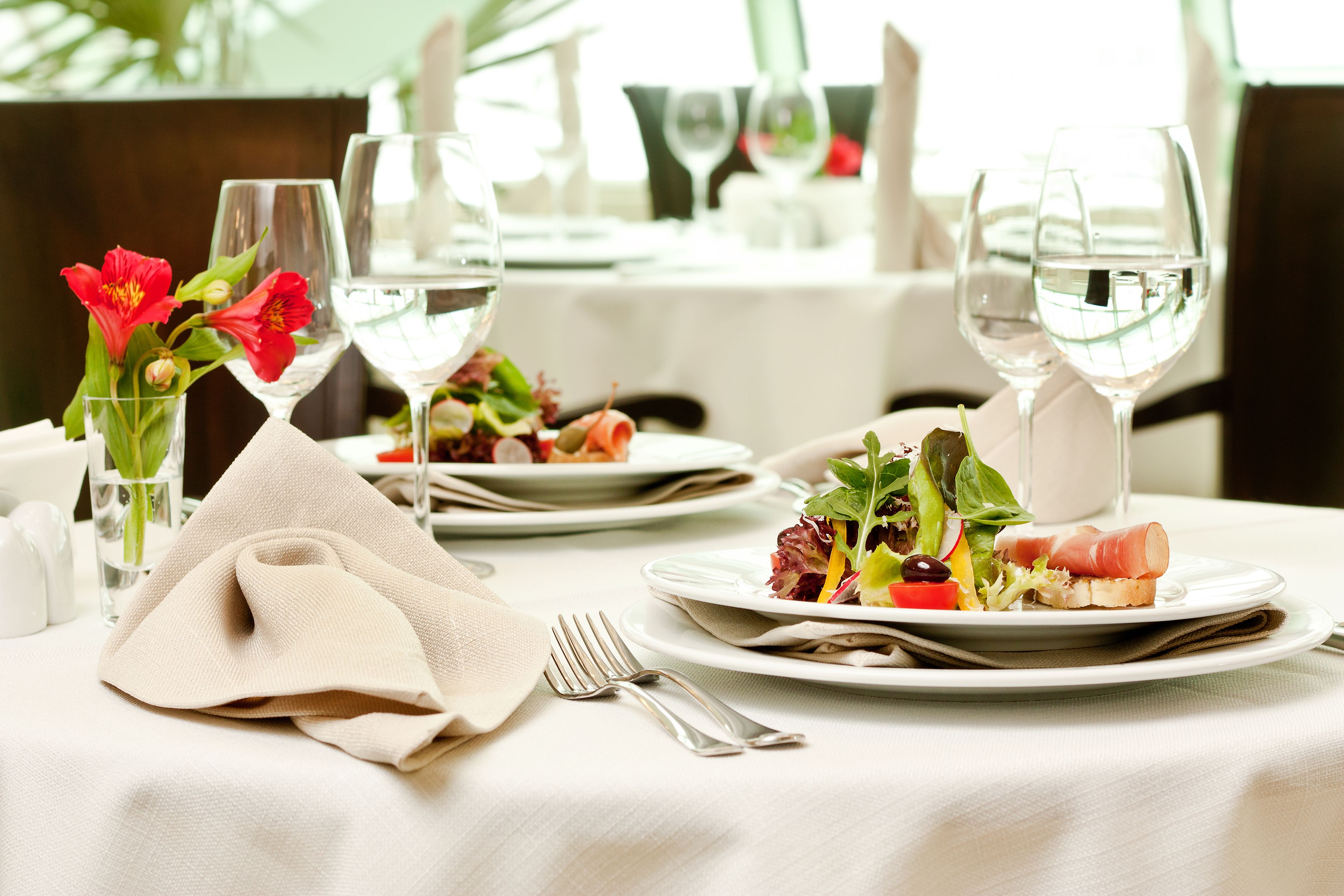 A dining table set with plates of food, wine glasses, and a vase with flowers.