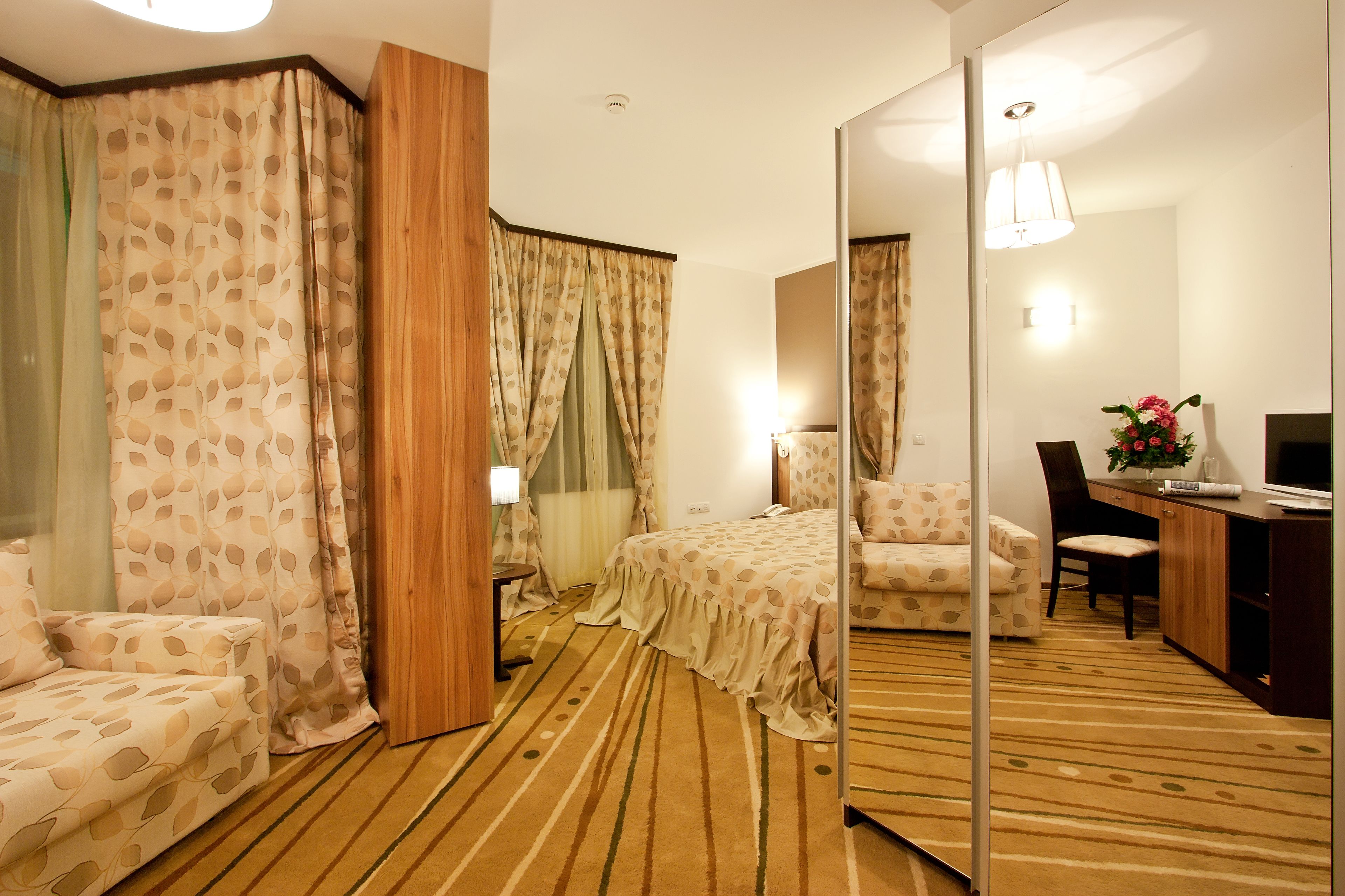 Una habitación de hotel con cama, escritorio, silla, espejo y lámpara.