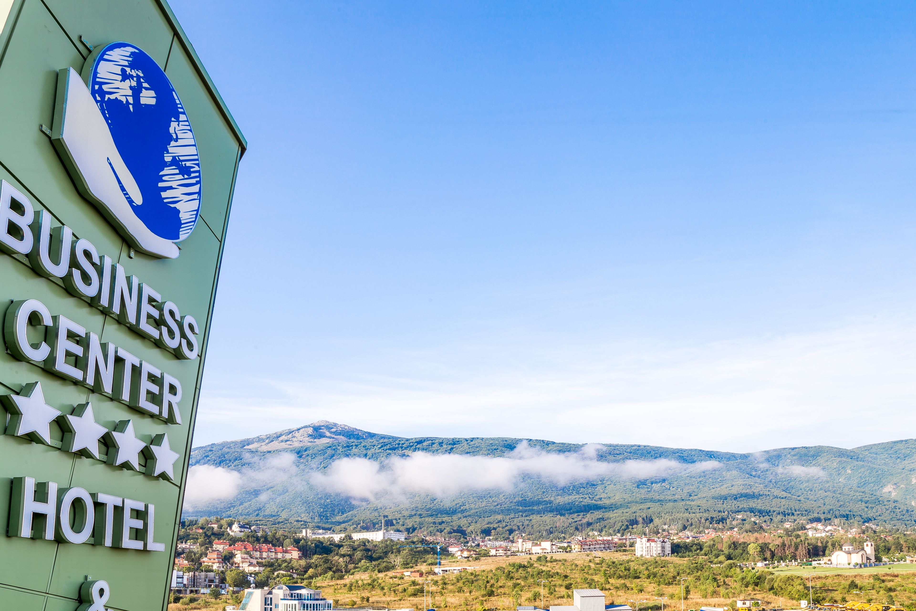 Señal de un hotel con centro de negocios y vista a un pueblo y montañas al fondo.
