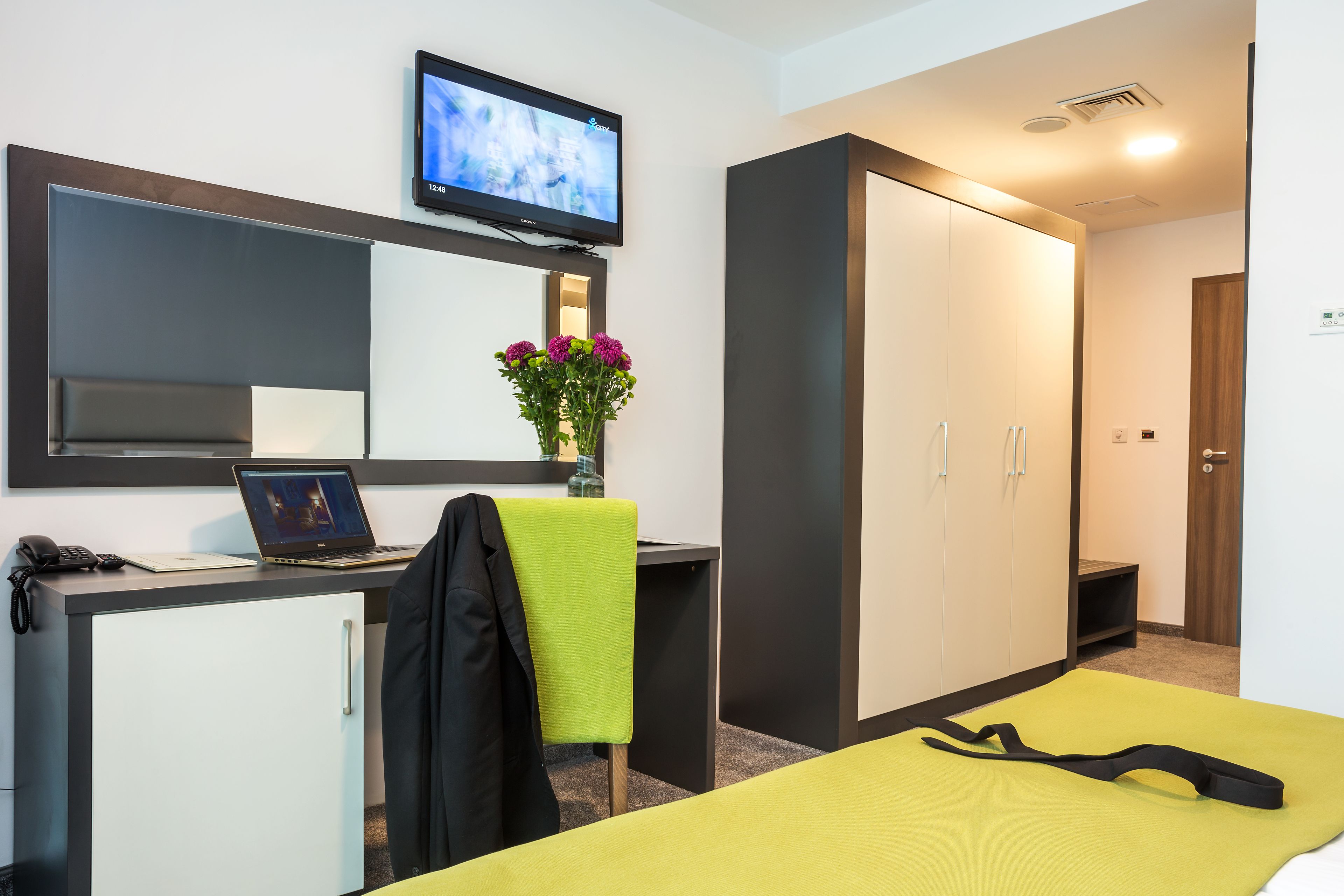 Una habitación de hotel con escritorio, computadora portátil, televisor, cama y armario.