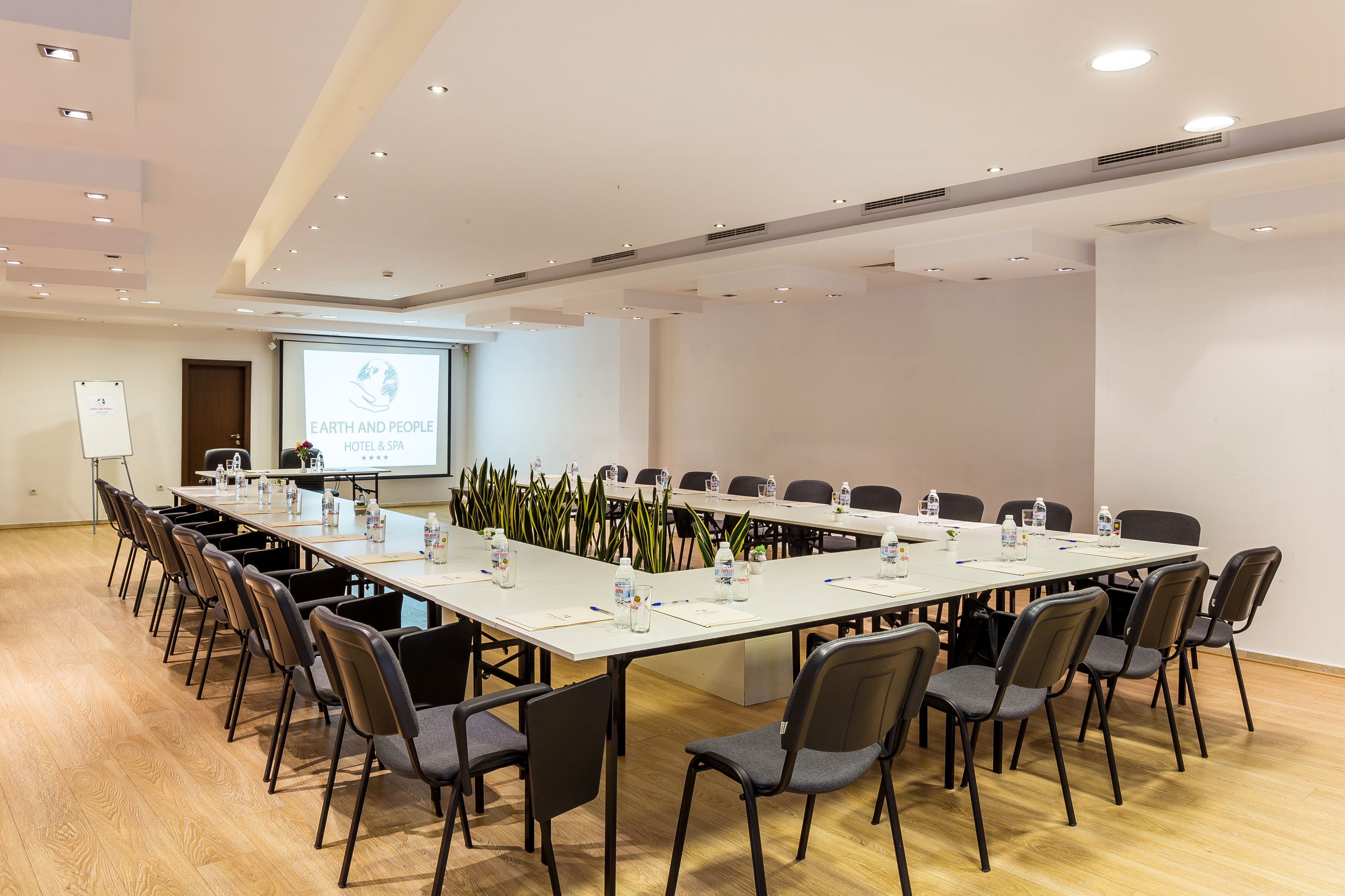 Una sala de conferencias con una larga mesa, sillas, una pantalla de proyector y una pizarra.