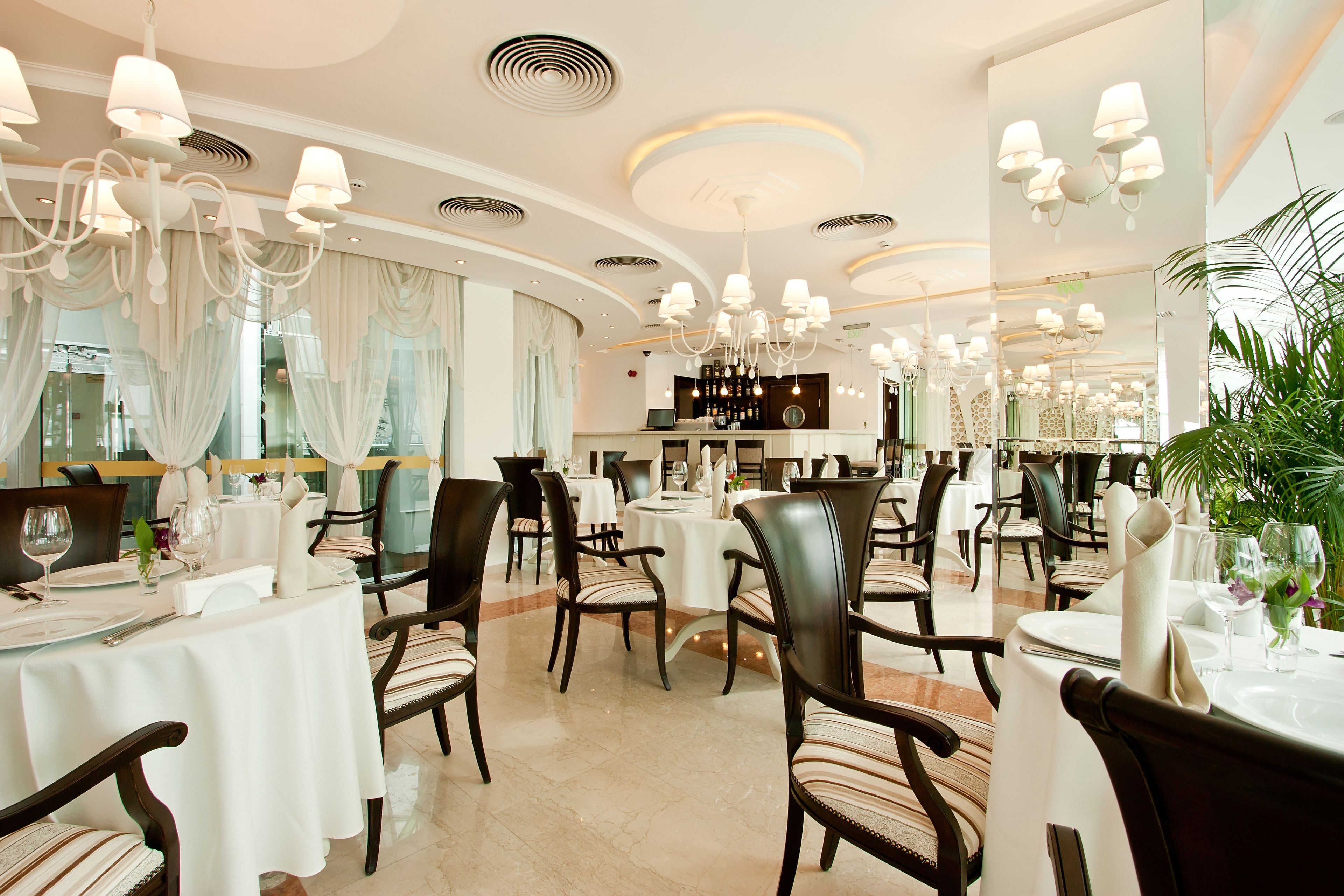 A restaurant with round tables, dark chairs, and chandeliers.