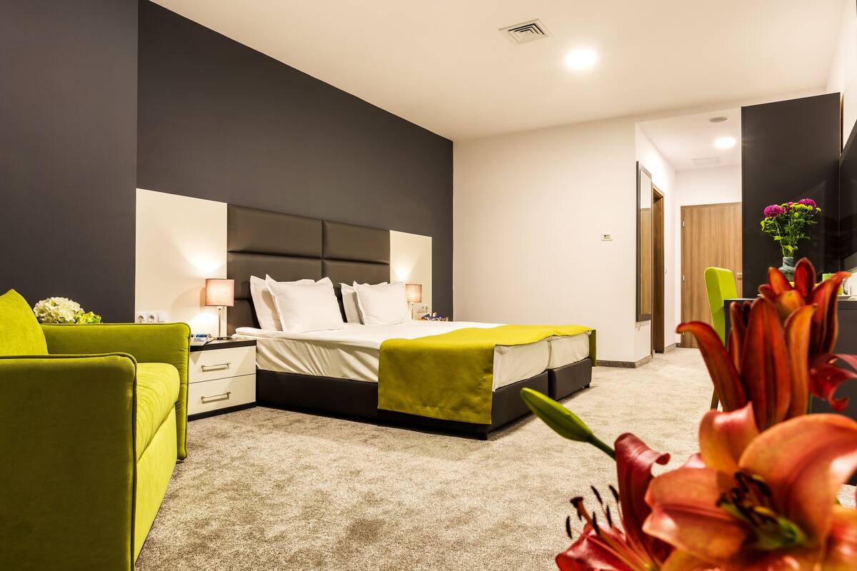 A modern hotel room with a large bed, a green armchair, a nightstand, and a desk.