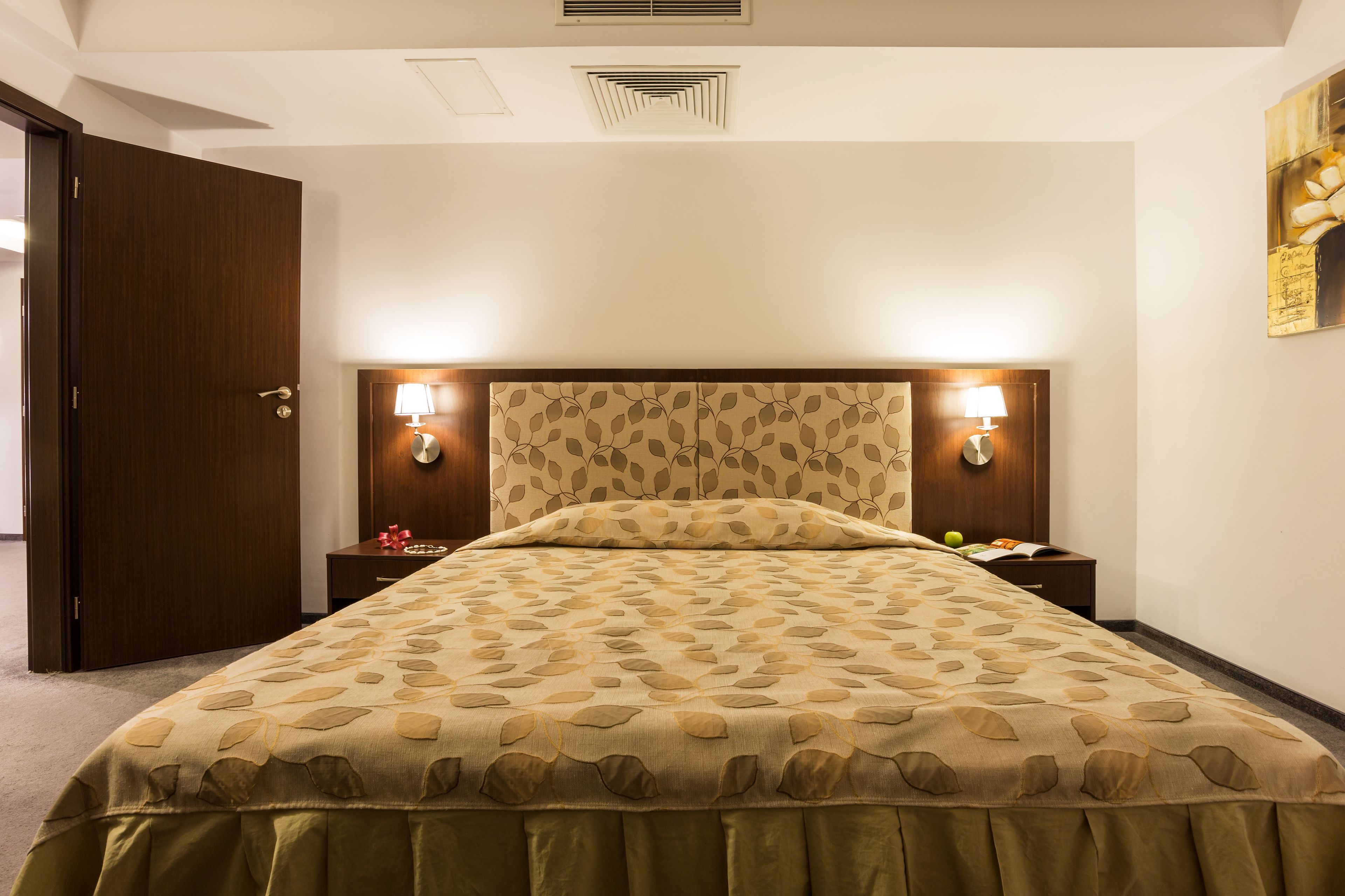 Een hotelkamer met een groot bed, twee bedlampen, een nachtkastje en een deur.