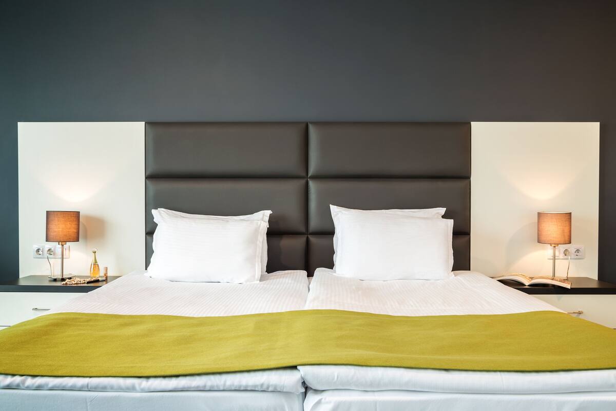 A double bed with a green throw blanket, two white pillows, and a dark headboard.